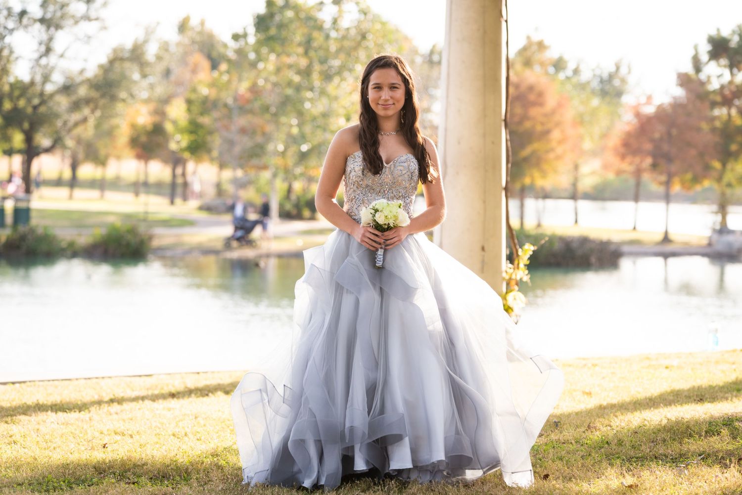 Bride in flowing white dress poses by column with lake and autumn foliage in background.