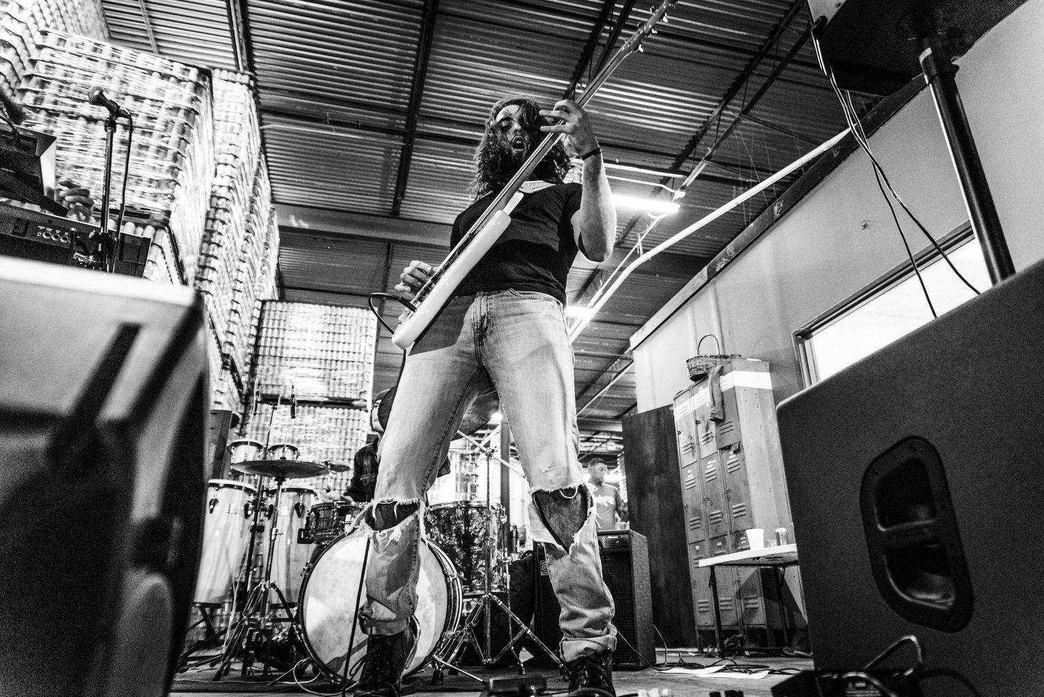 Low angle black and white shot of musician playing guitar on stage with equipment visible.