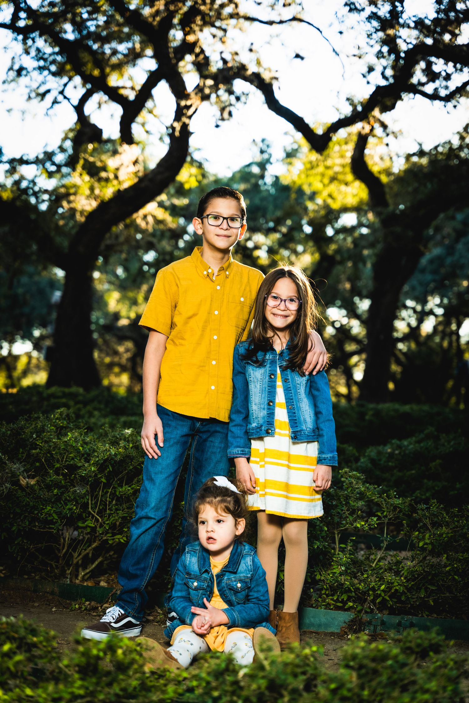 A yellow and denim-clad family portrait taken outdoors with trees and natural lighting in the background.