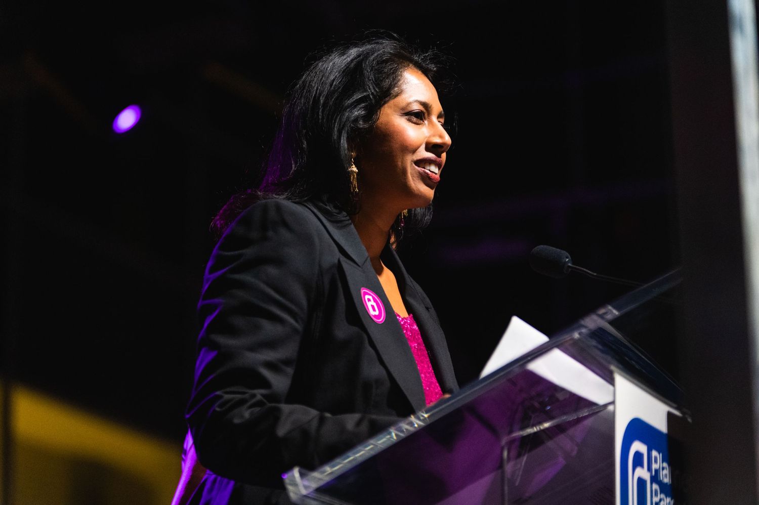 Speaker in black blazer addresses audience from Planned Parenthood podium on stage.
