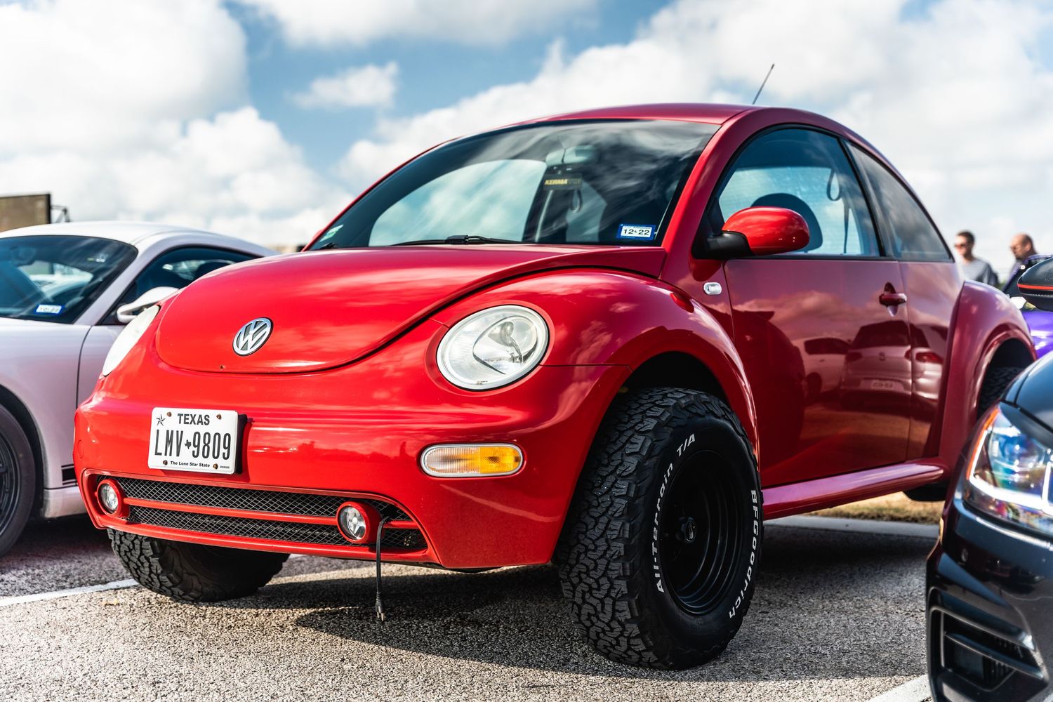 Red Volkswagen New Beetle with black wheels and off-road style modifications.