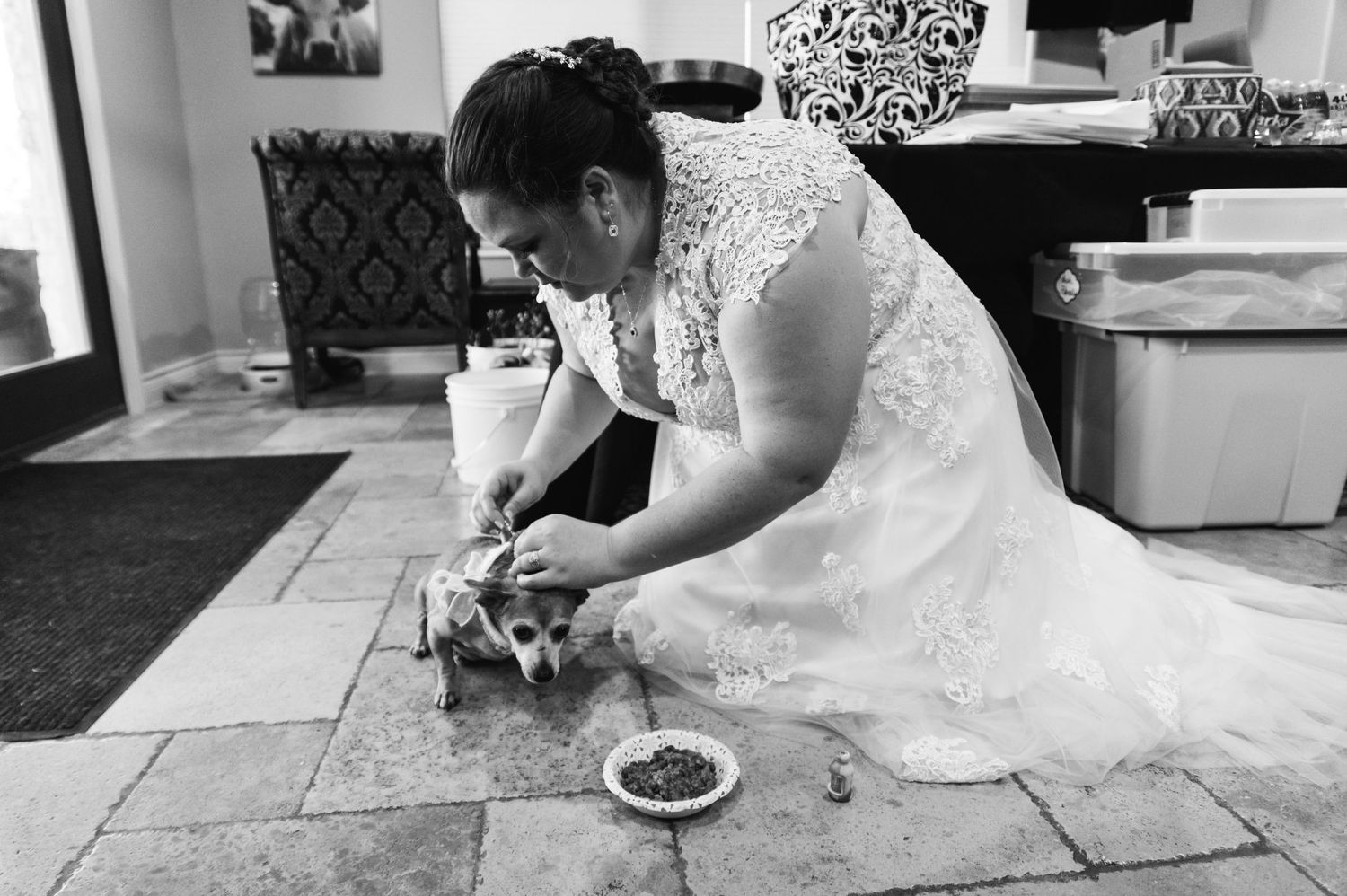 Black and white photo of person in wedding dress tending to small animal on tiled floor.