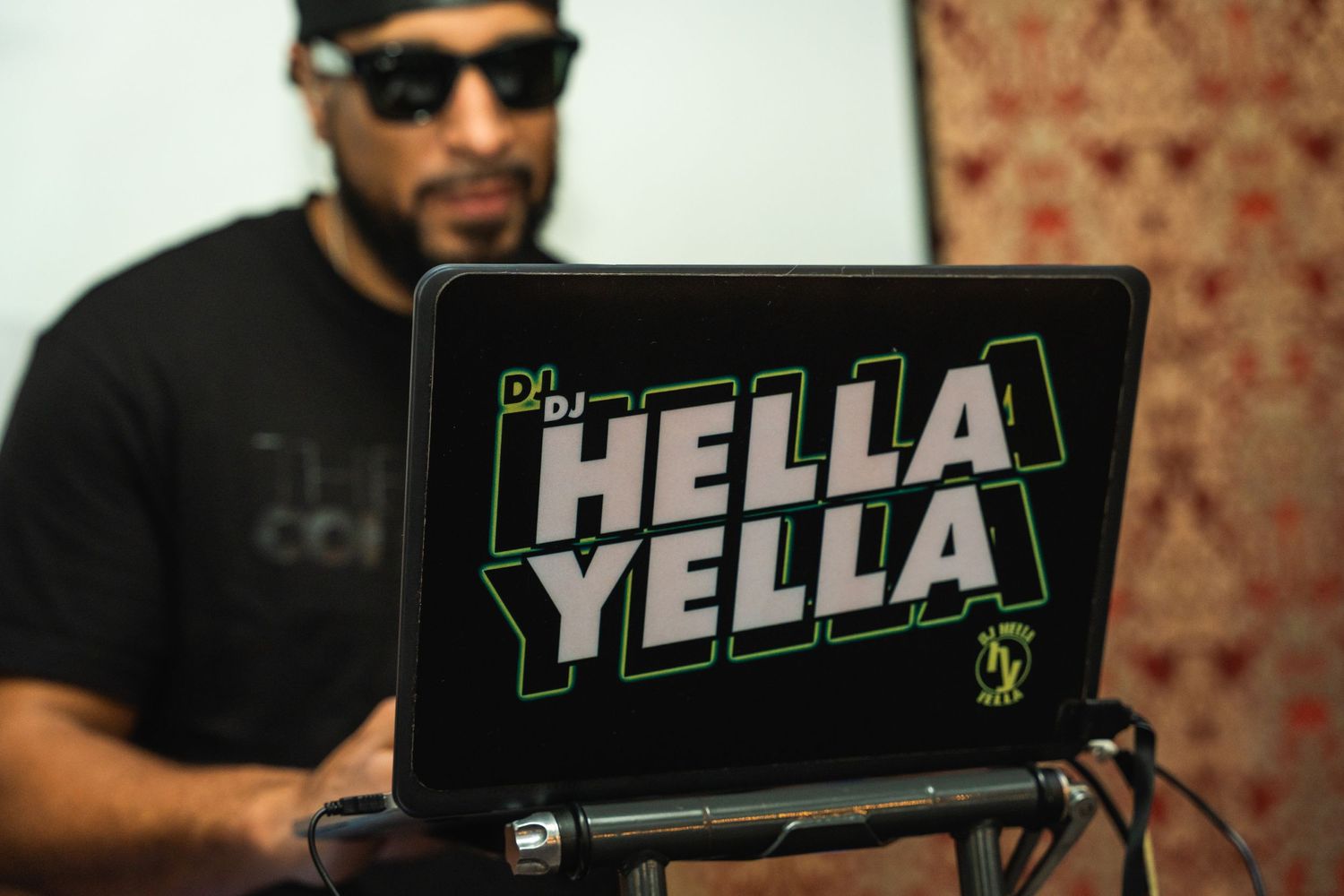 A laptop displays the text 'HELLA YELLA' in bright green lettering.