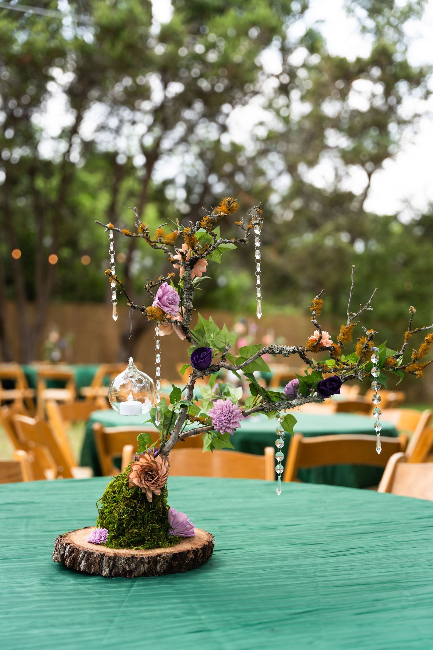 Enchanting woodland-themed centerpiece with crystal drops and fresh flowers on green tablecloth.