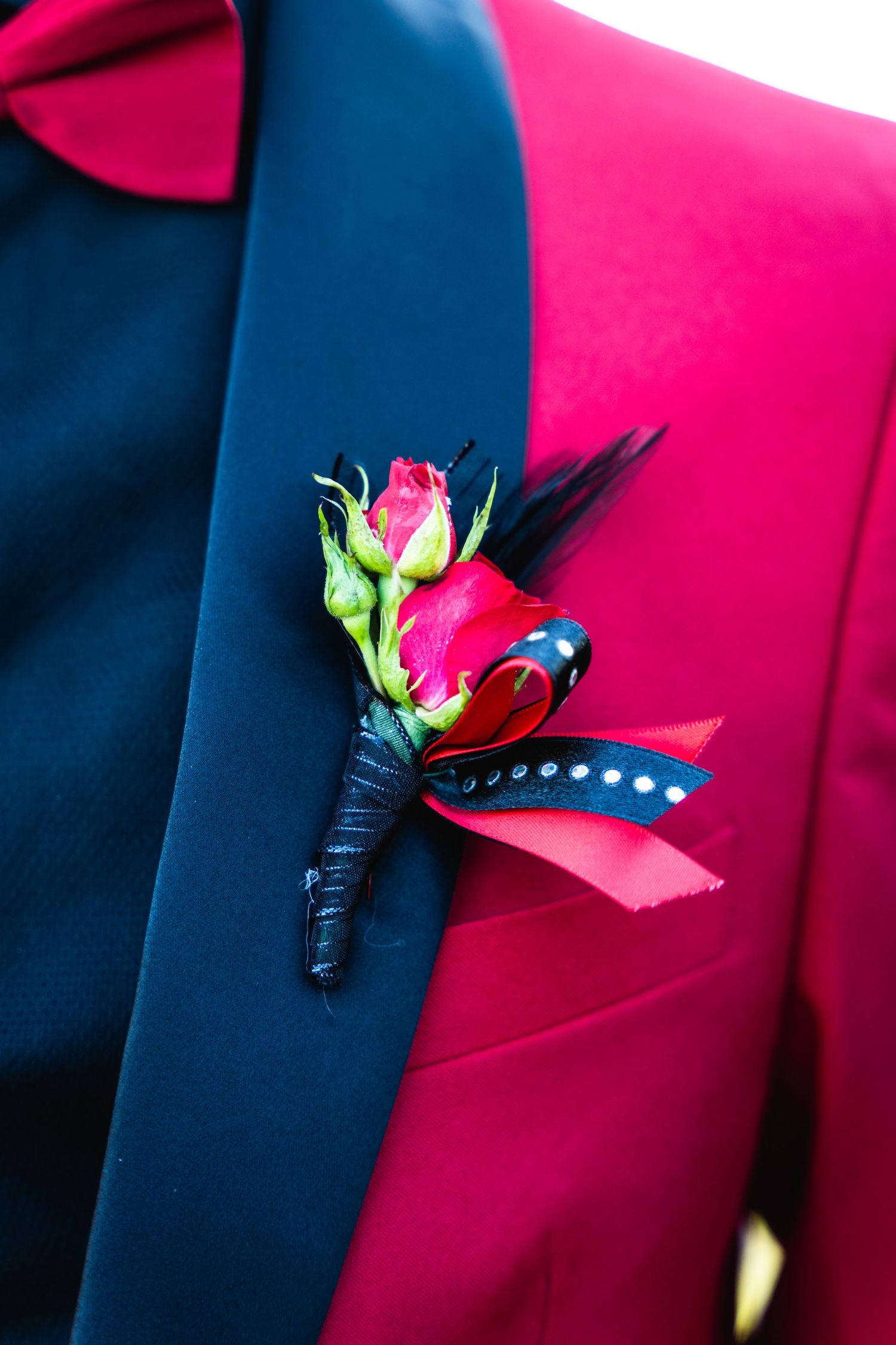 A vibrant pink boutonniere with red roses and blue accents pinned to a navy suit jacket.