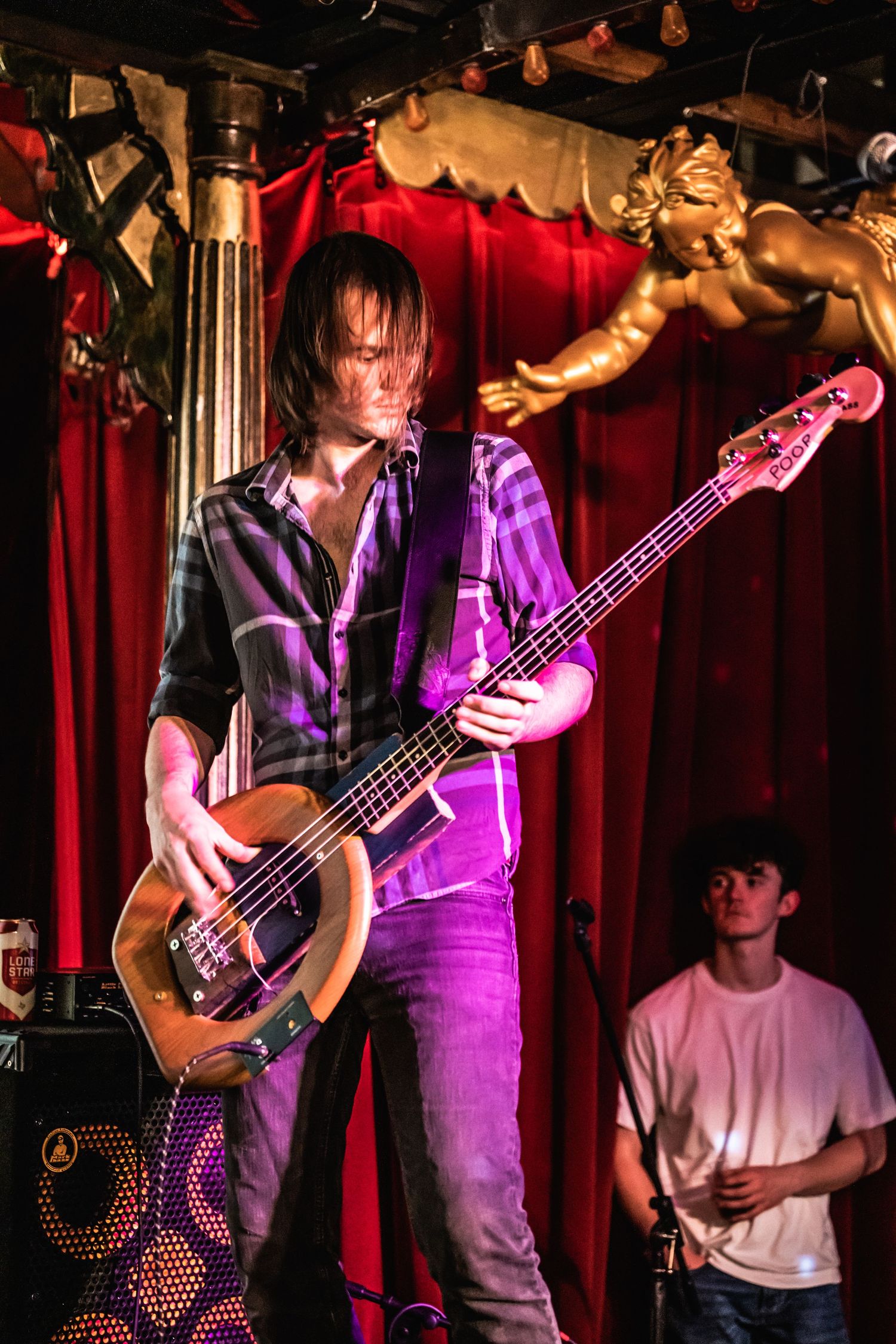 Bass player performing on stage with purple lighting and red curtain backdrop.