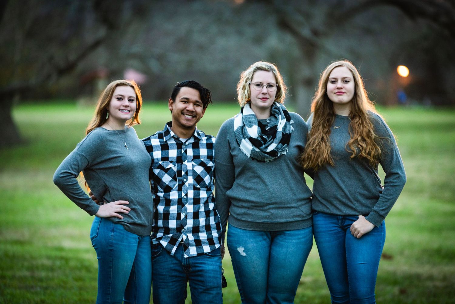 Group photo of four people in coordinated casual outfits standing together outdoors on grass.