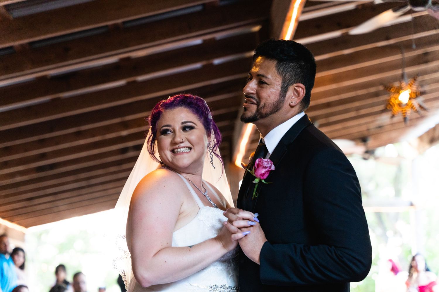 A joyful first dance at a wedding reception under wooden beams.