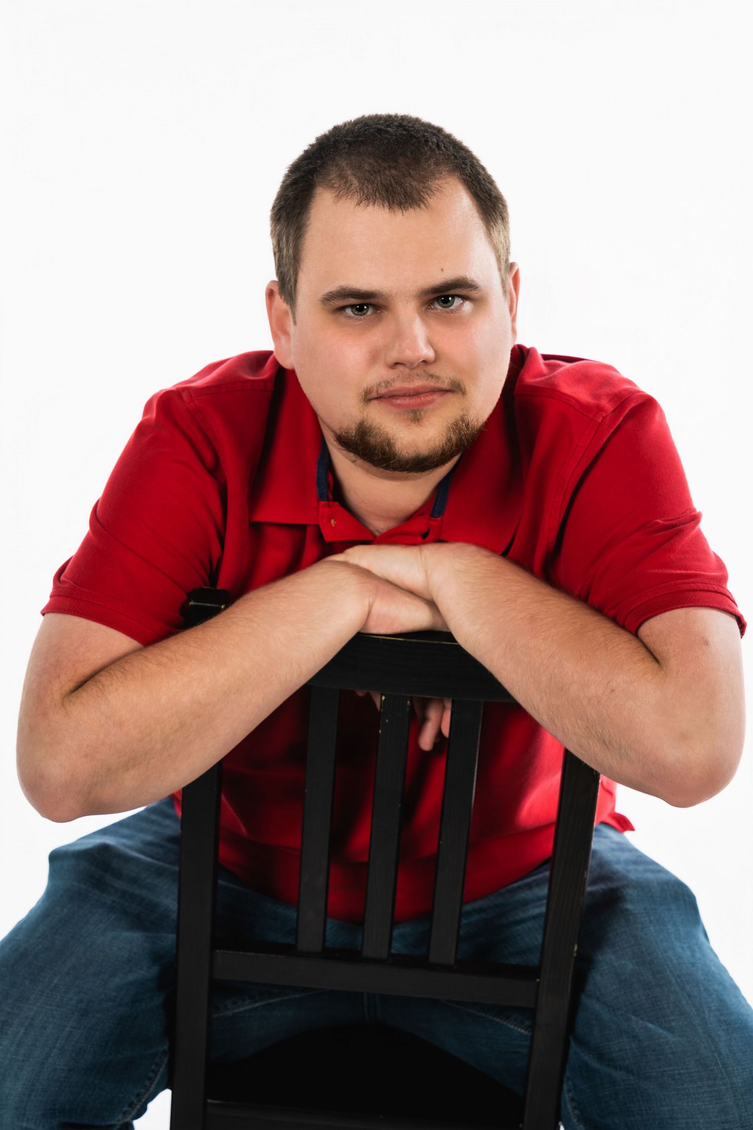 Portrait of person in red polo shirt sitting backwards on chair against white background.