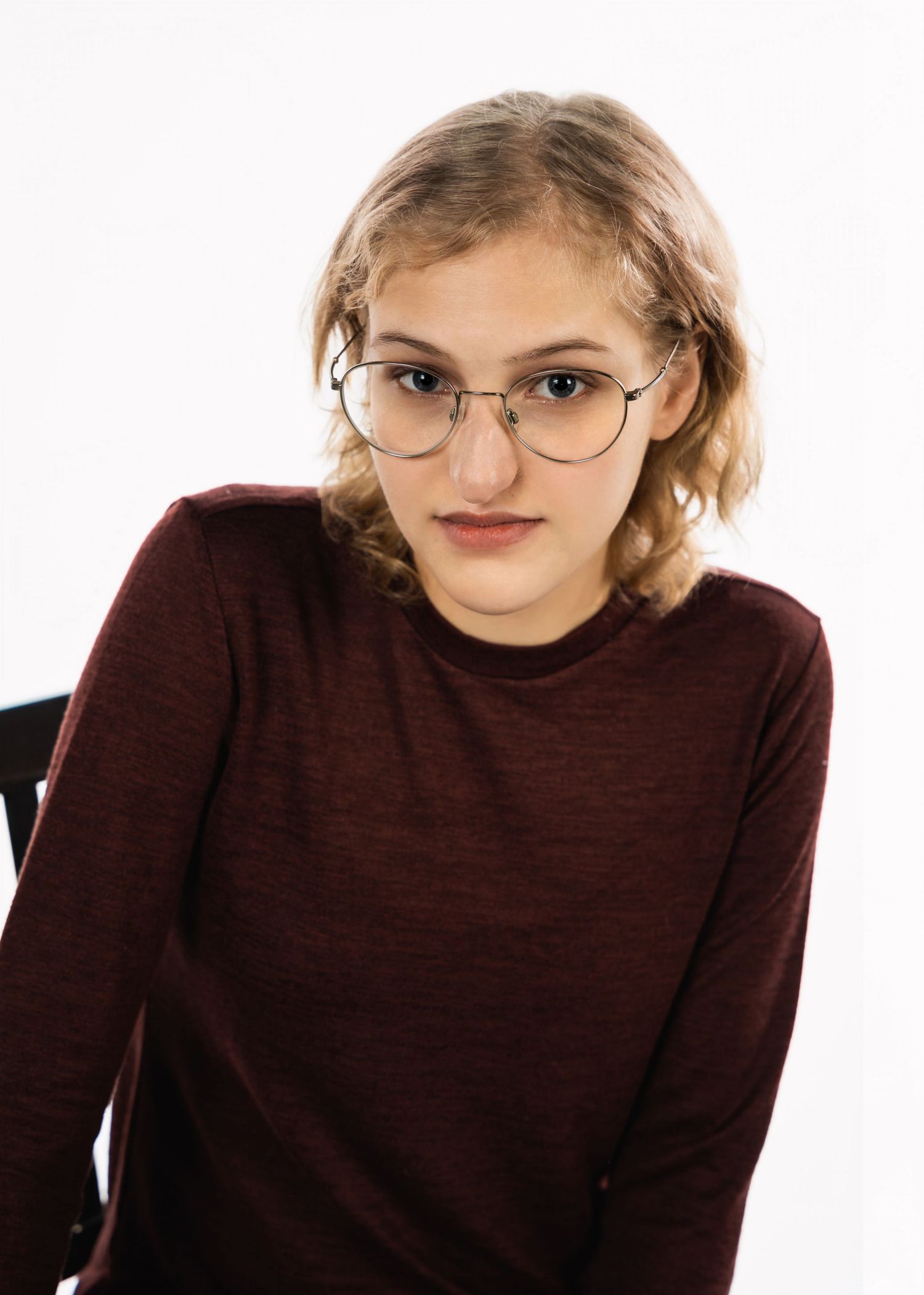 Portrait shot of woman in burgundy sweater and glasses against white background.