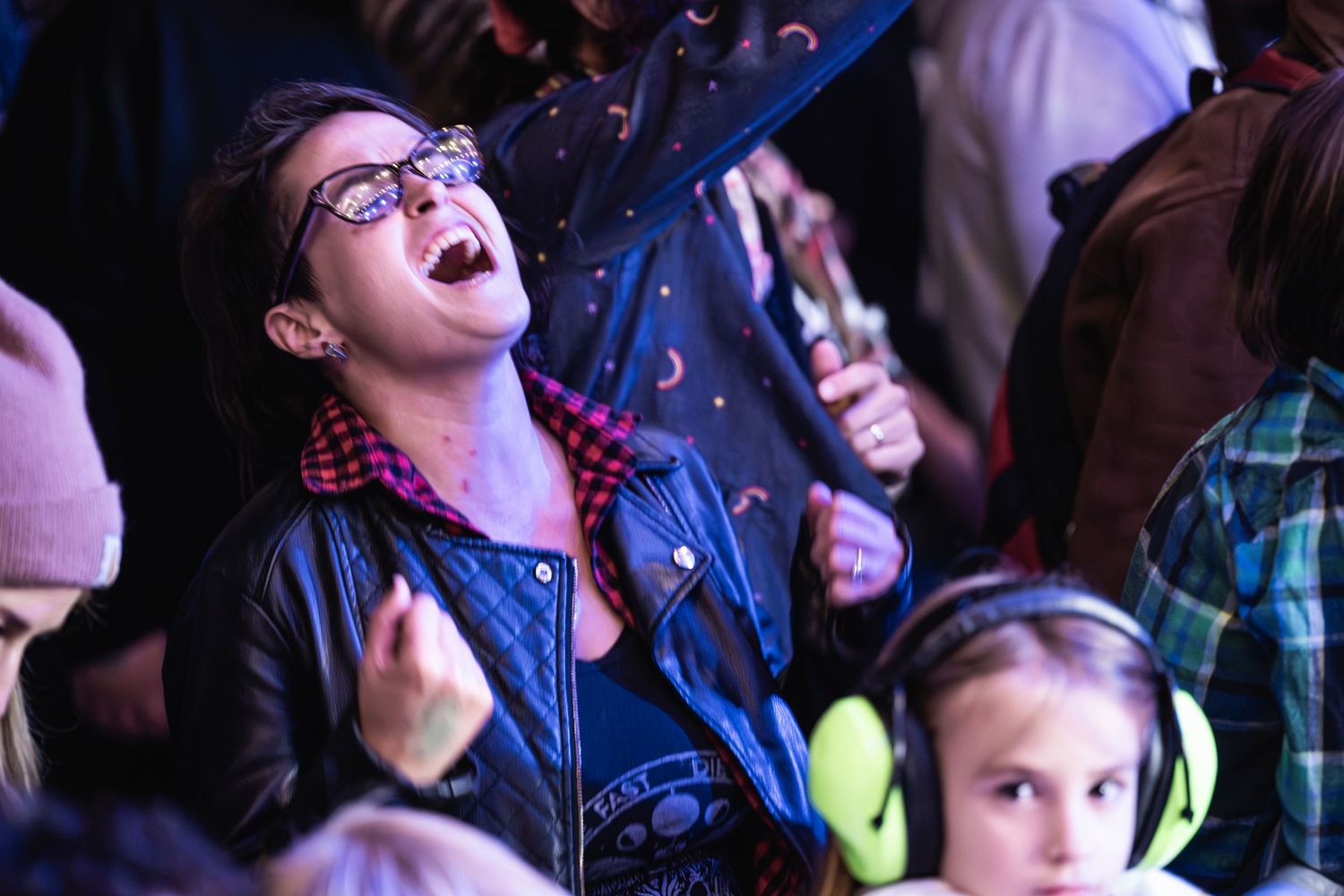 Enthusiastic concert goer wearing glasses and leather jacket caught mid-song in the crowd.