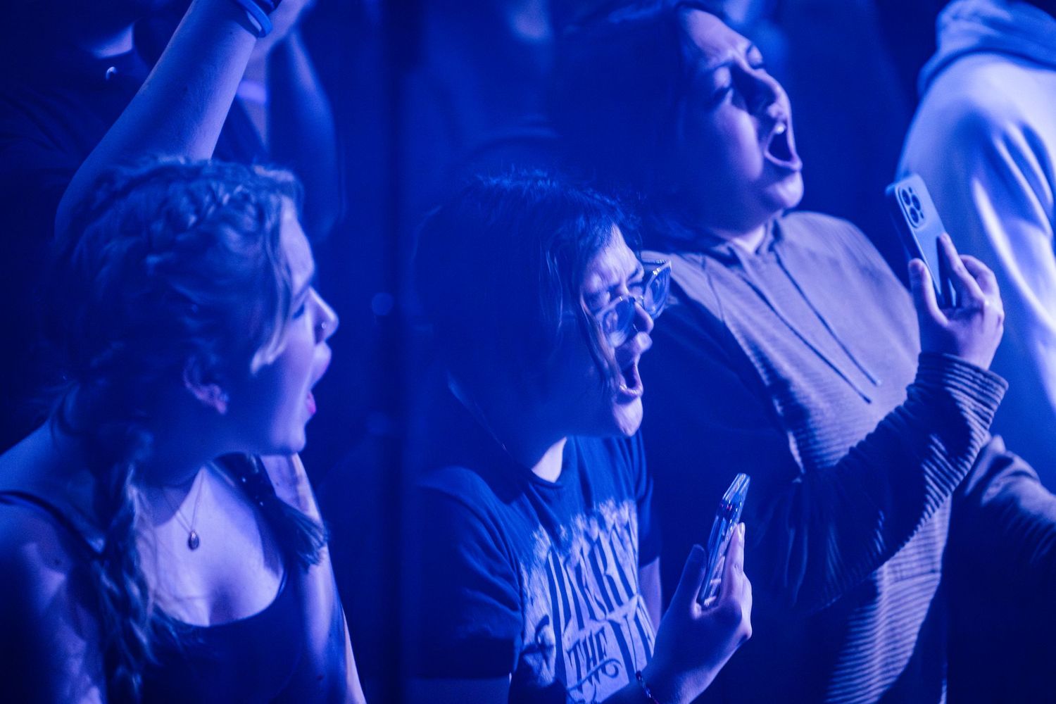 Passionate fans react emotionally to a performance under blue concert lighting.