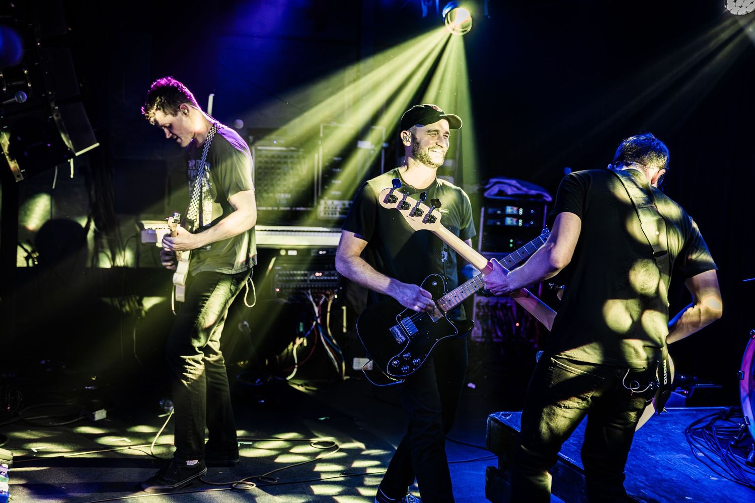 Rock band members play instruments under dramatic stage lighting during live performance.