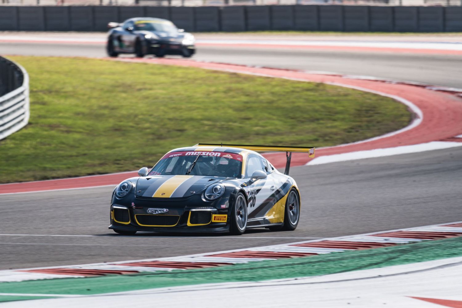 Black and yellow racing Porsche navigates a curve on a professional racetrack during competition.