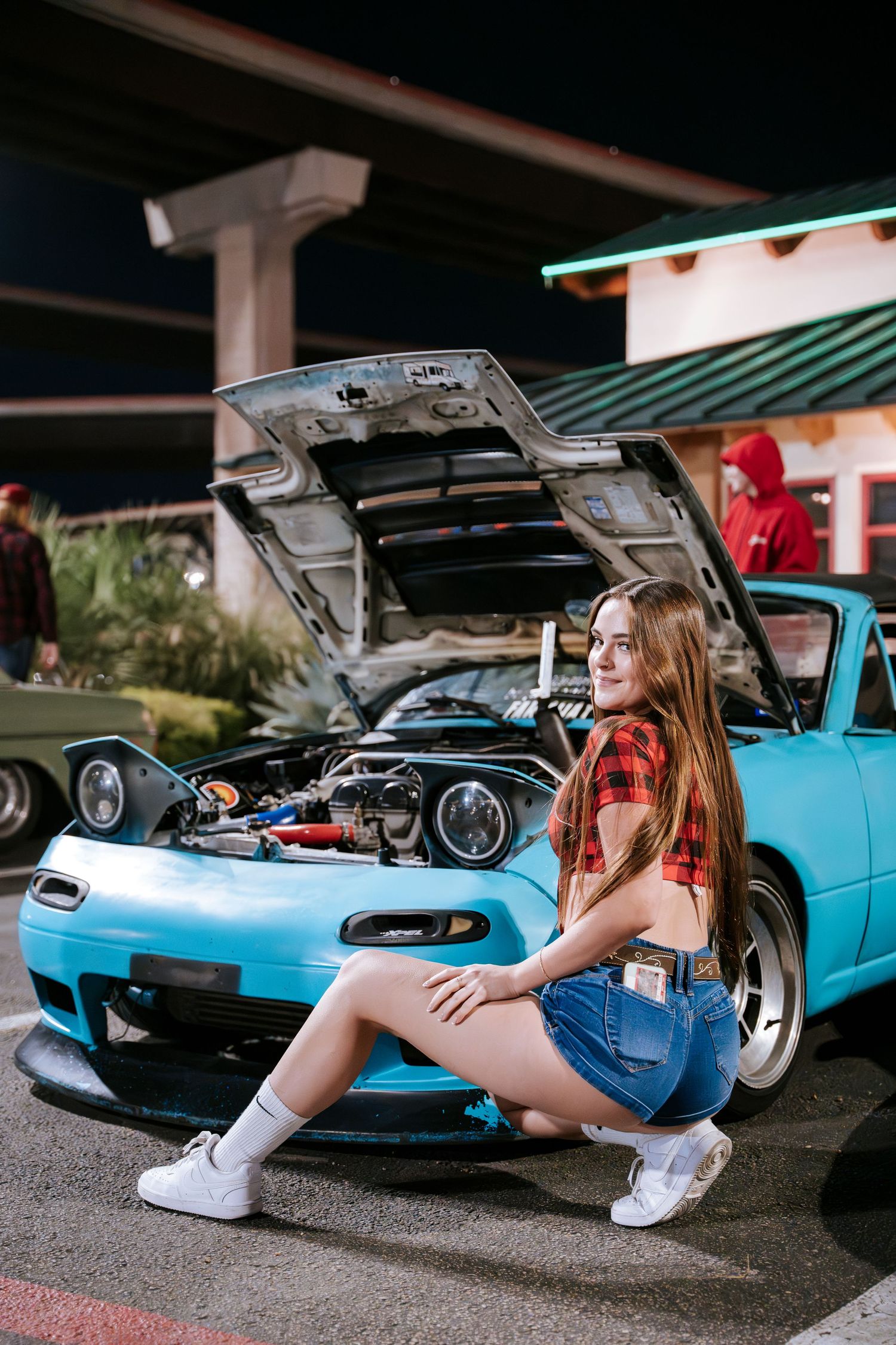 Light blue Mazda Miata with open hood at nighttime car meet.