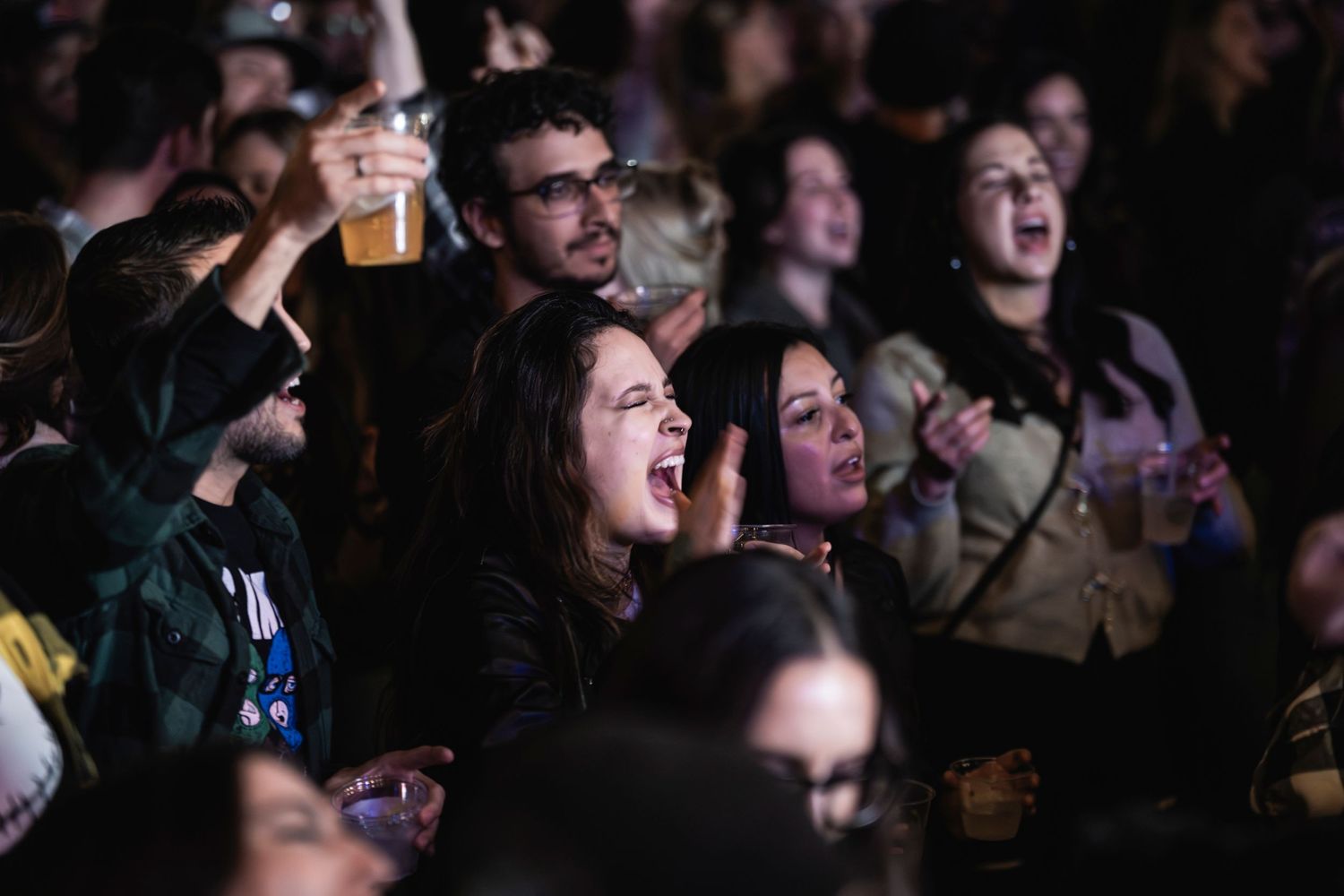 Energetic crowd members singing along and raising drinks during a live music performance.