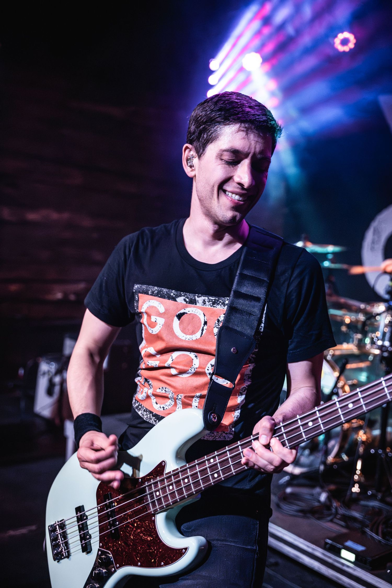 Bass guitarist performing with white instrument under blue stage lighting.