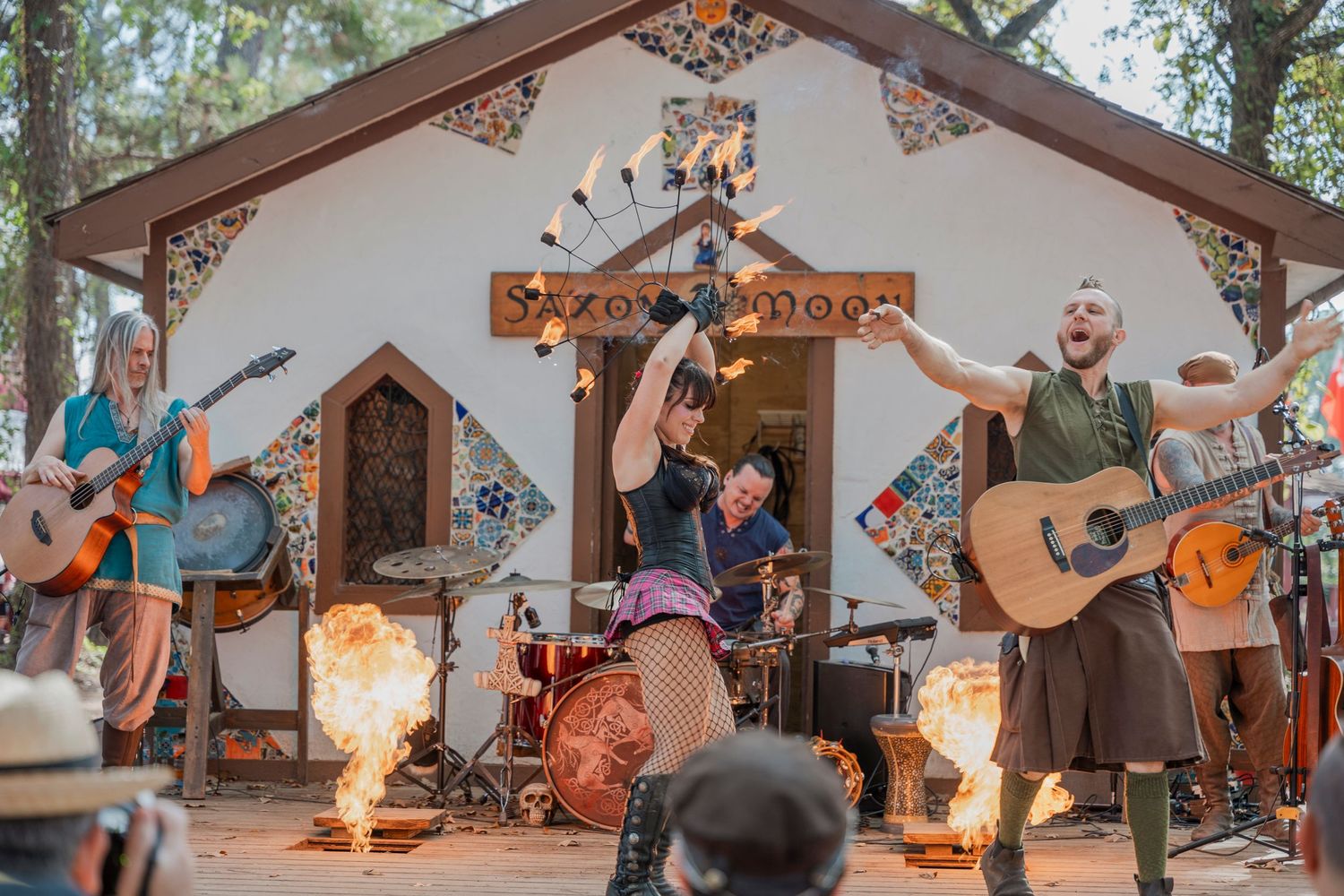 Folk band performs on decorated stage with fire effects at renaissance festival.