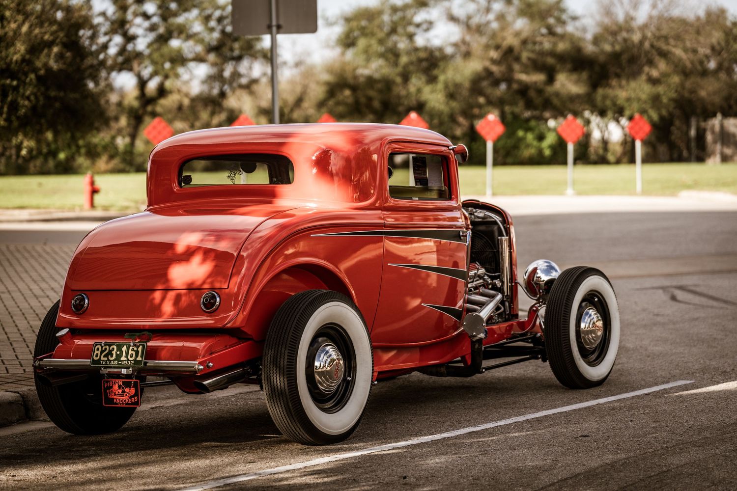 Red vintage hot rod coupe with white wall tires parked in lot.