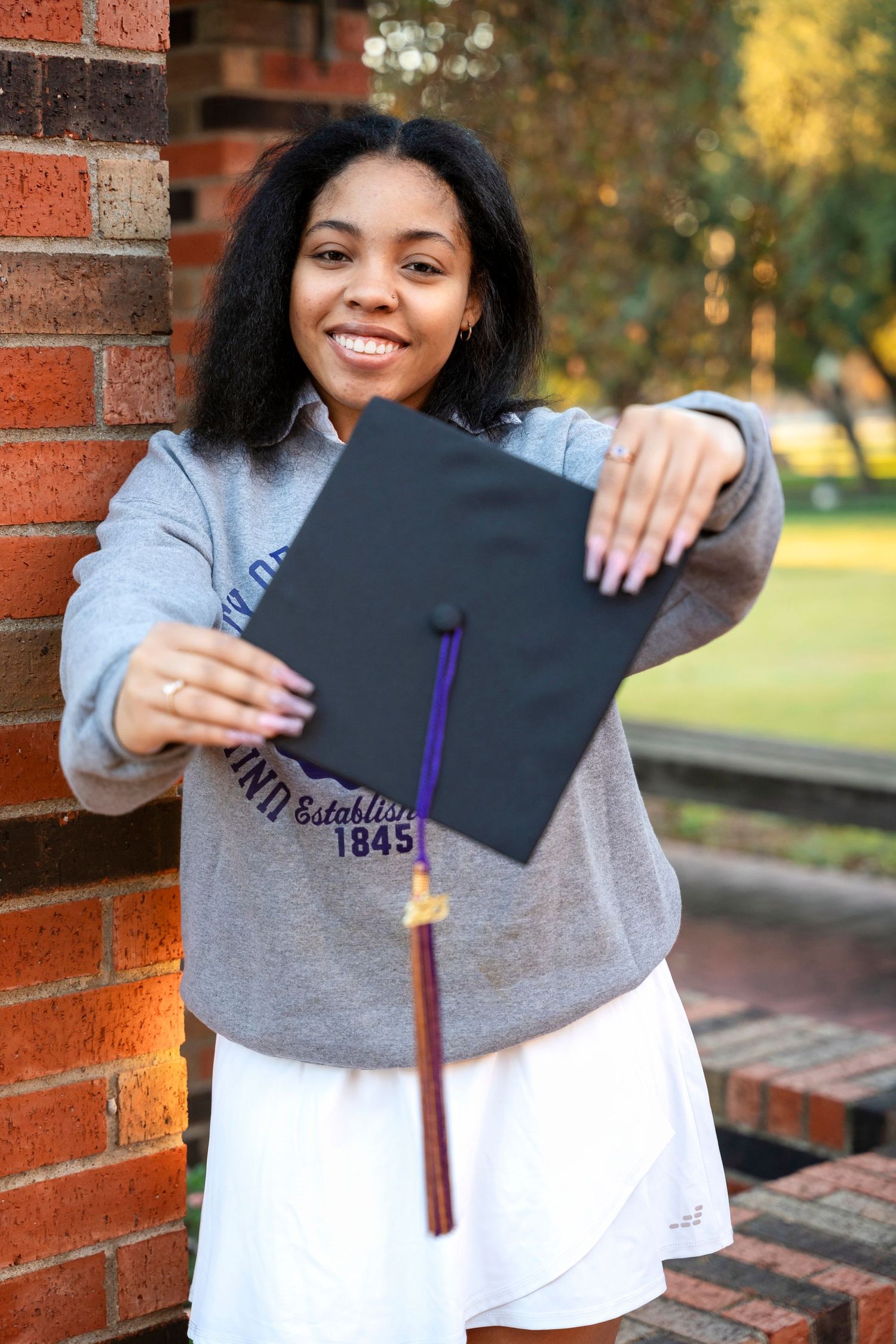 Graduate displays diploma holder while wearing grey university sweatshirt.