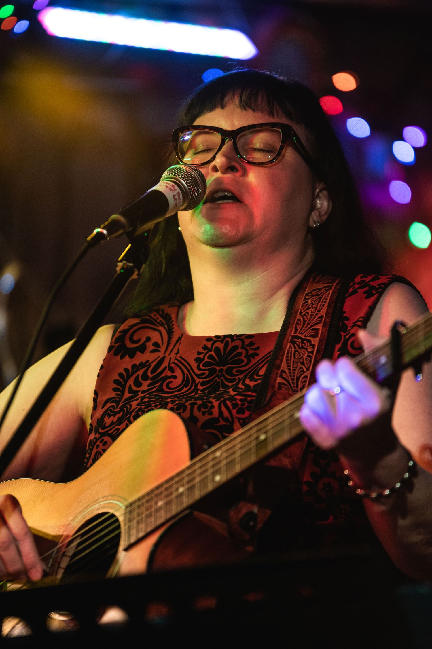 Musician playing acoustic guitar and singing under colorful venue lighting.