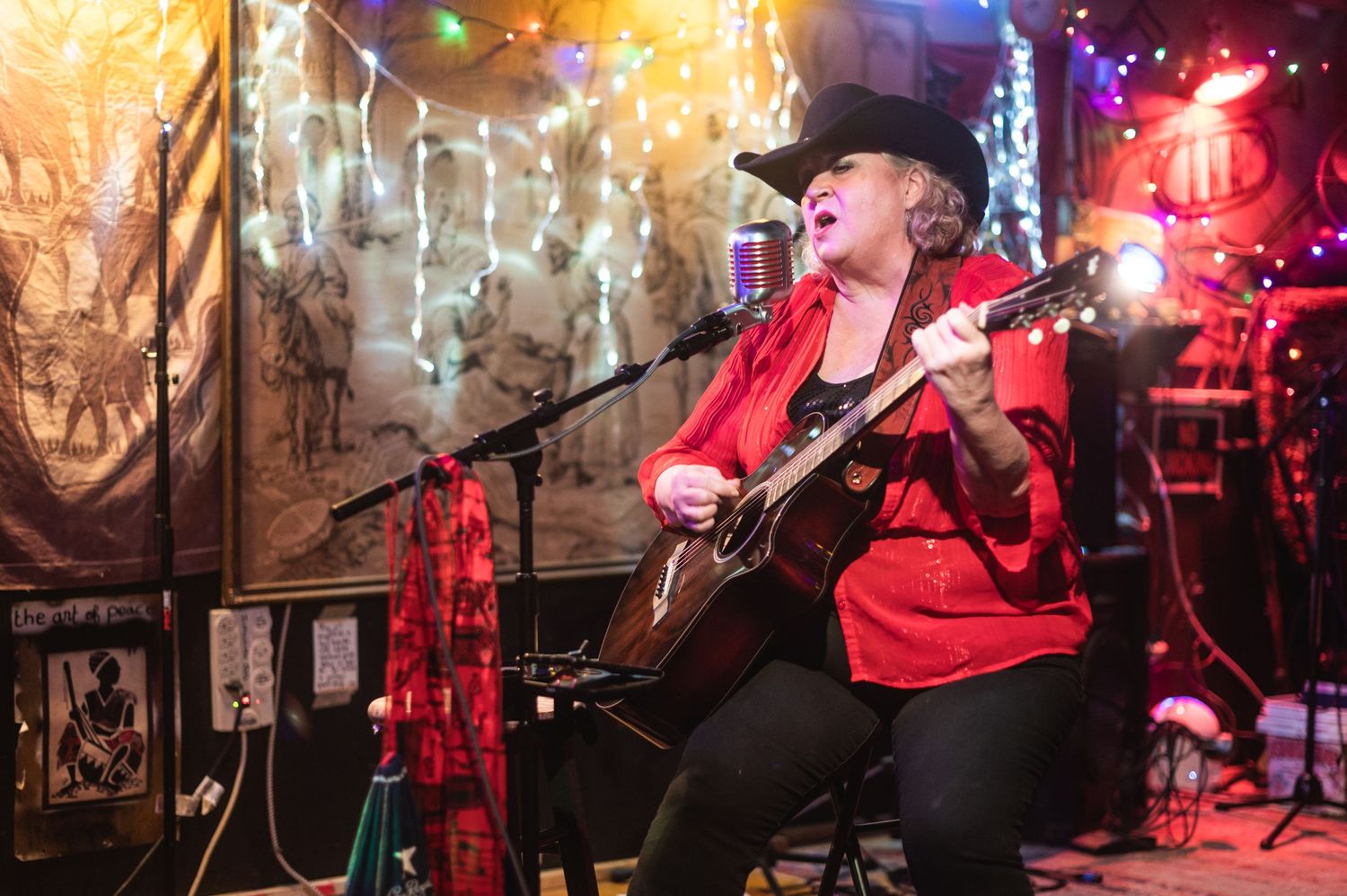 A performer plays acoustic guitar on stage with warm lighting and decorative backdrop.
