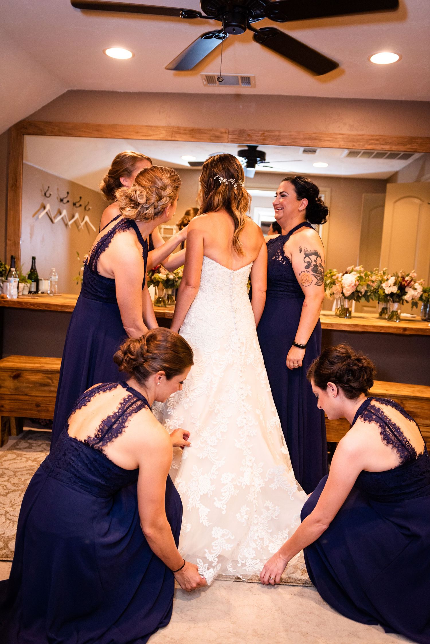 Wedding party helping with the bride's dress train in a warmly lit room.