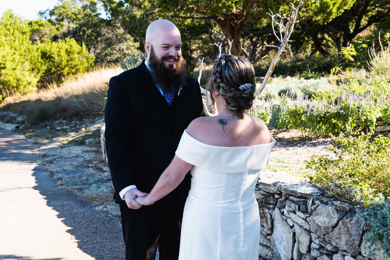 Couple shares an intimate moment during their wedding ceremony outdoors with stone wall and greenery in background.