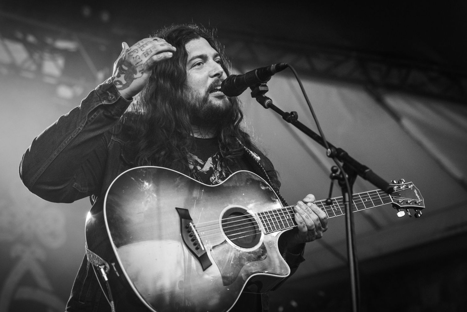 Musician playing acoustic guitar and singing into microphone during moody black and white performance.