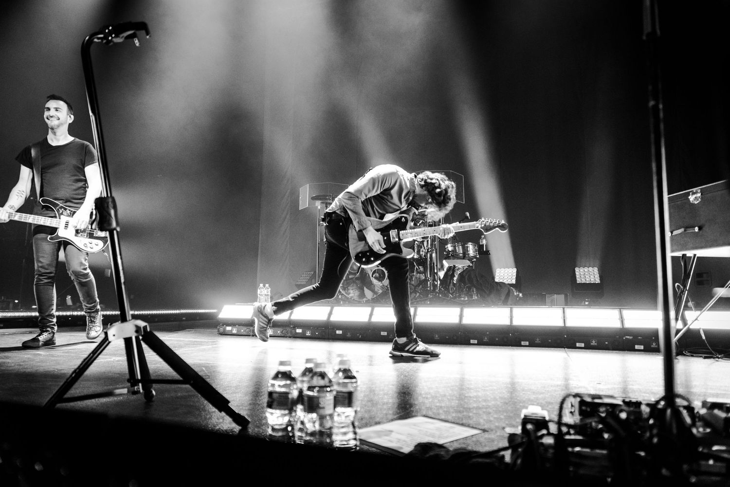 Black and white concert photo showing performers on stage with dramatic lighting and water bottles.