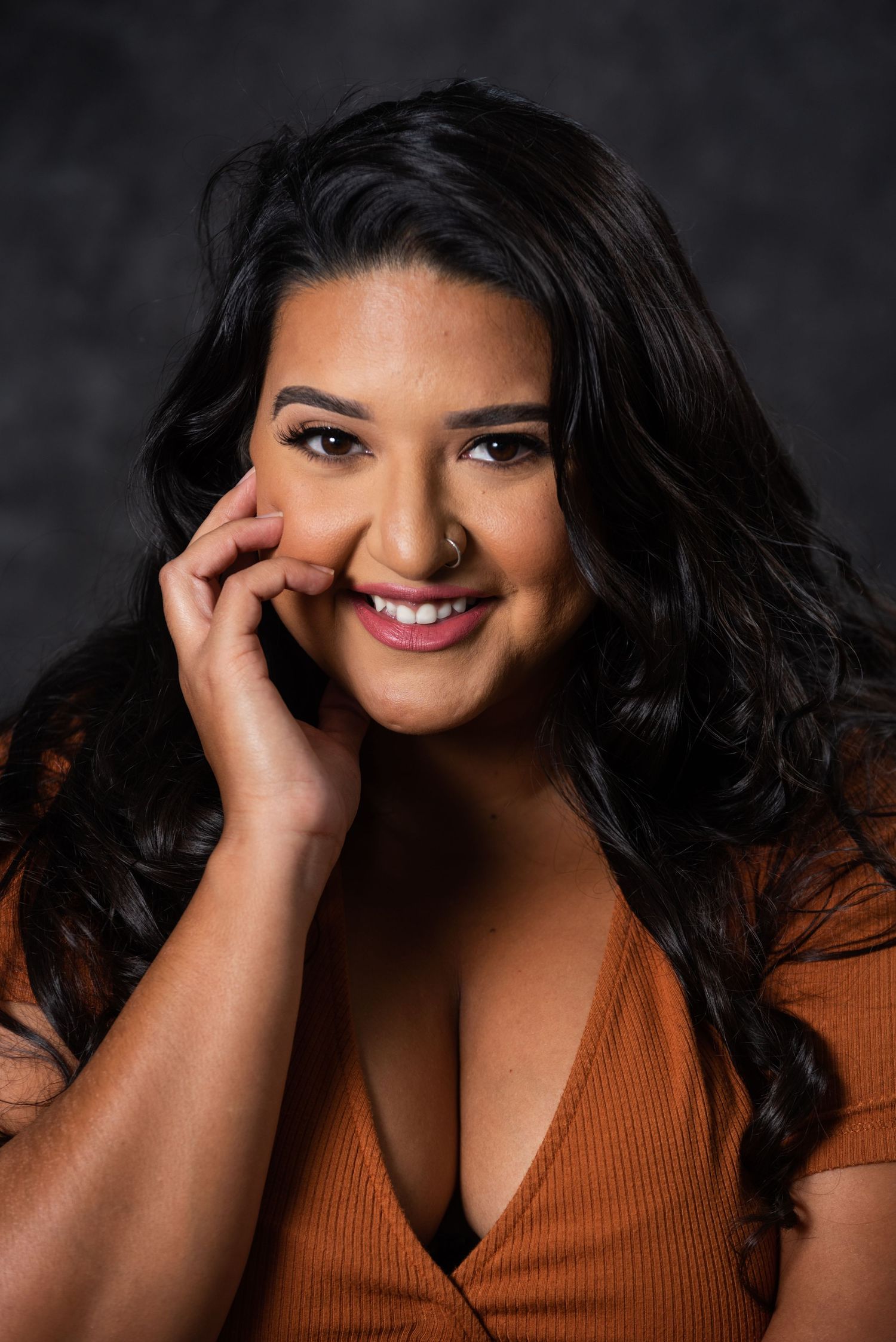 Glamour portrait of woman in orange top with natural makeup and wavy dark hair.