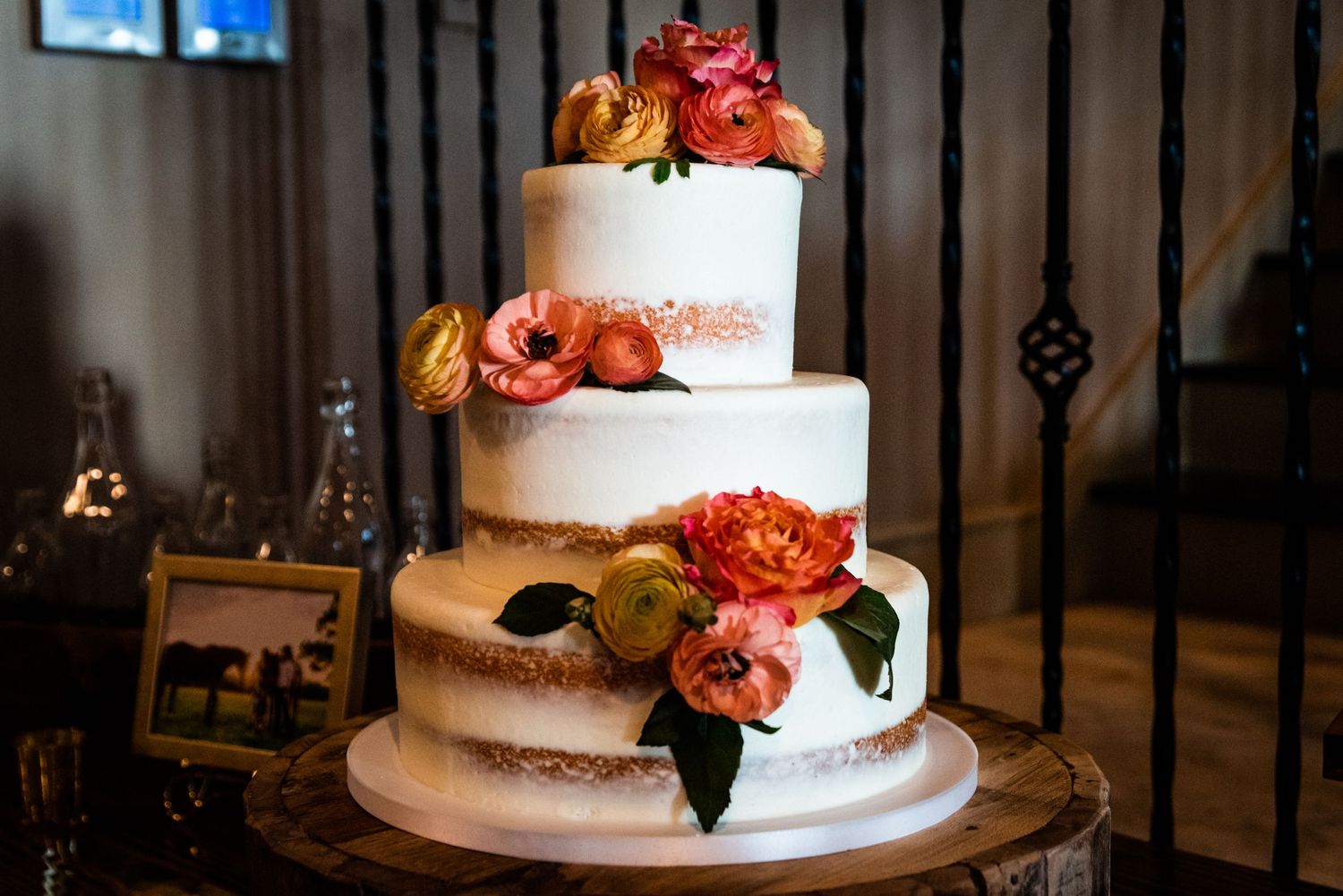 Multi-tiered white wedding cake decorated with coral and peach flowers on rustic wood stand.