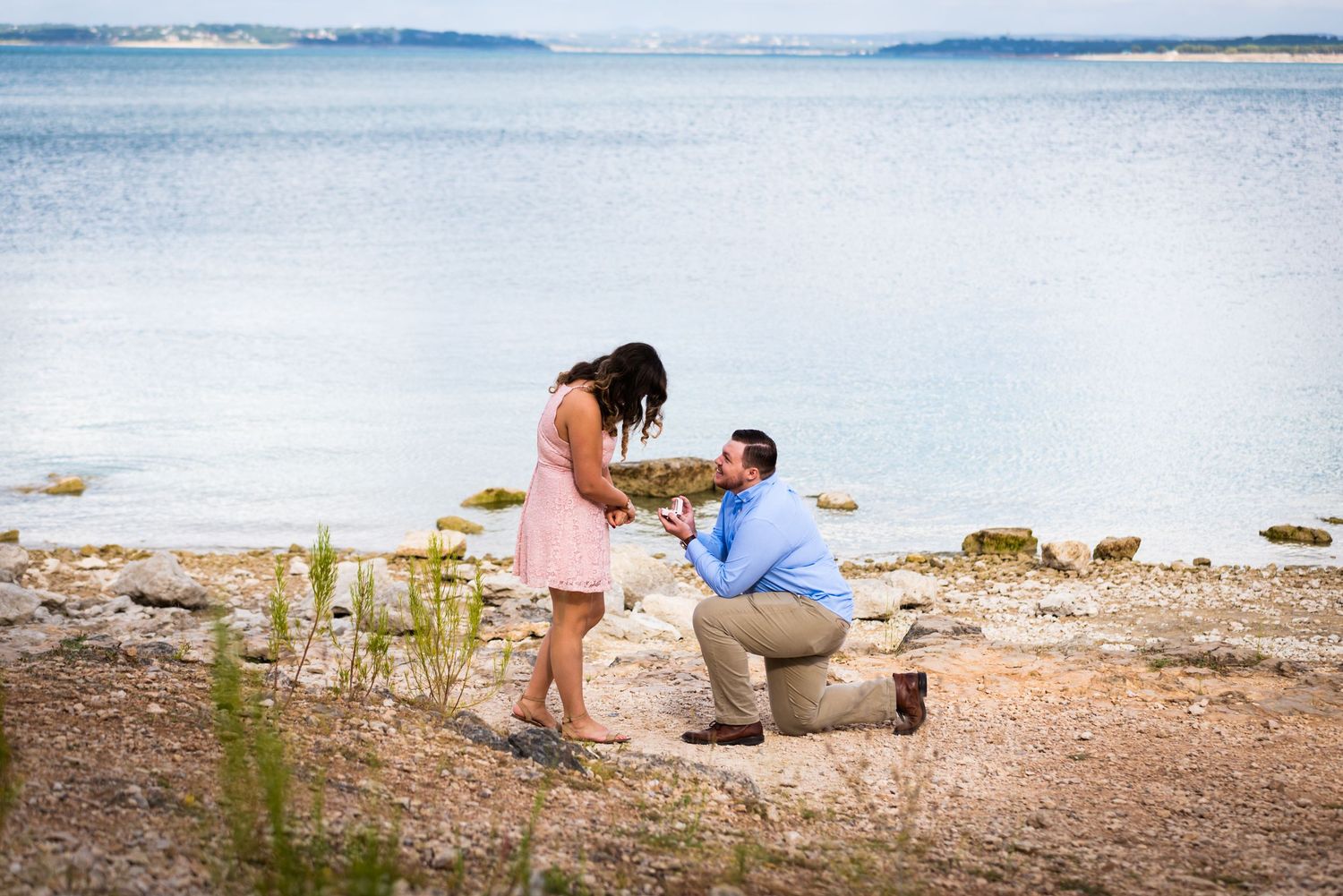 A special moment unfolds on a beach shoreline as a proposal takes place near the water.