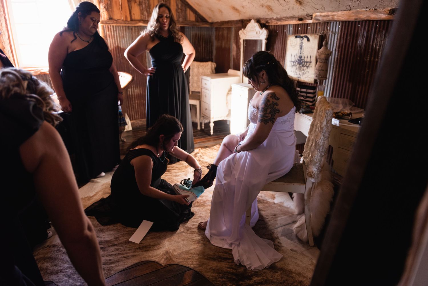 Wedding party helps with final dress preparations in rustic wooden room.