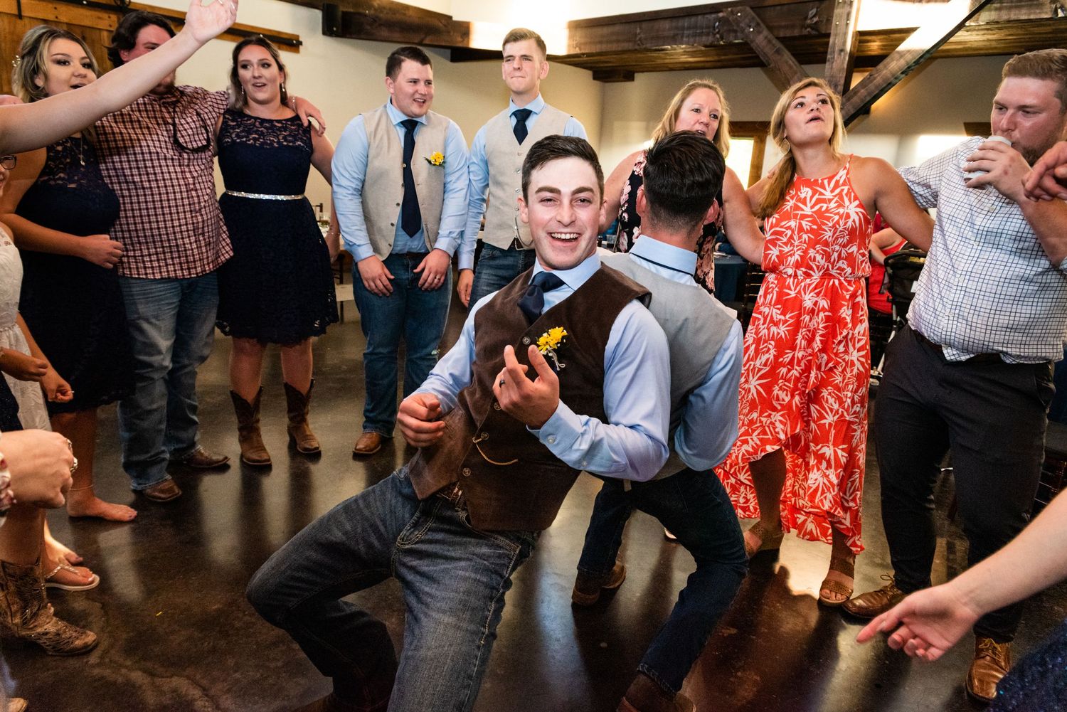 A guest performs an enthusiastic dance move while others cheer at a lively wedding reception.