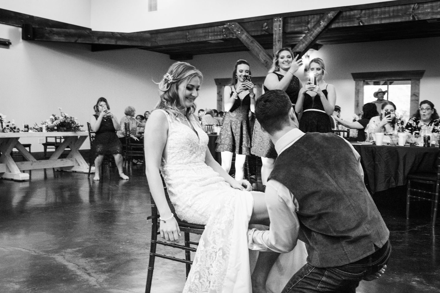 Traditional wedding garter removal ceremony taking place during reception with guests watching in background.