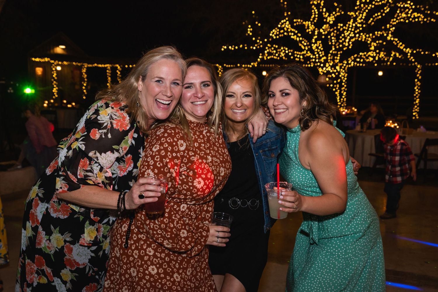 Group of wedding guests posing together at night under illuminated trees.