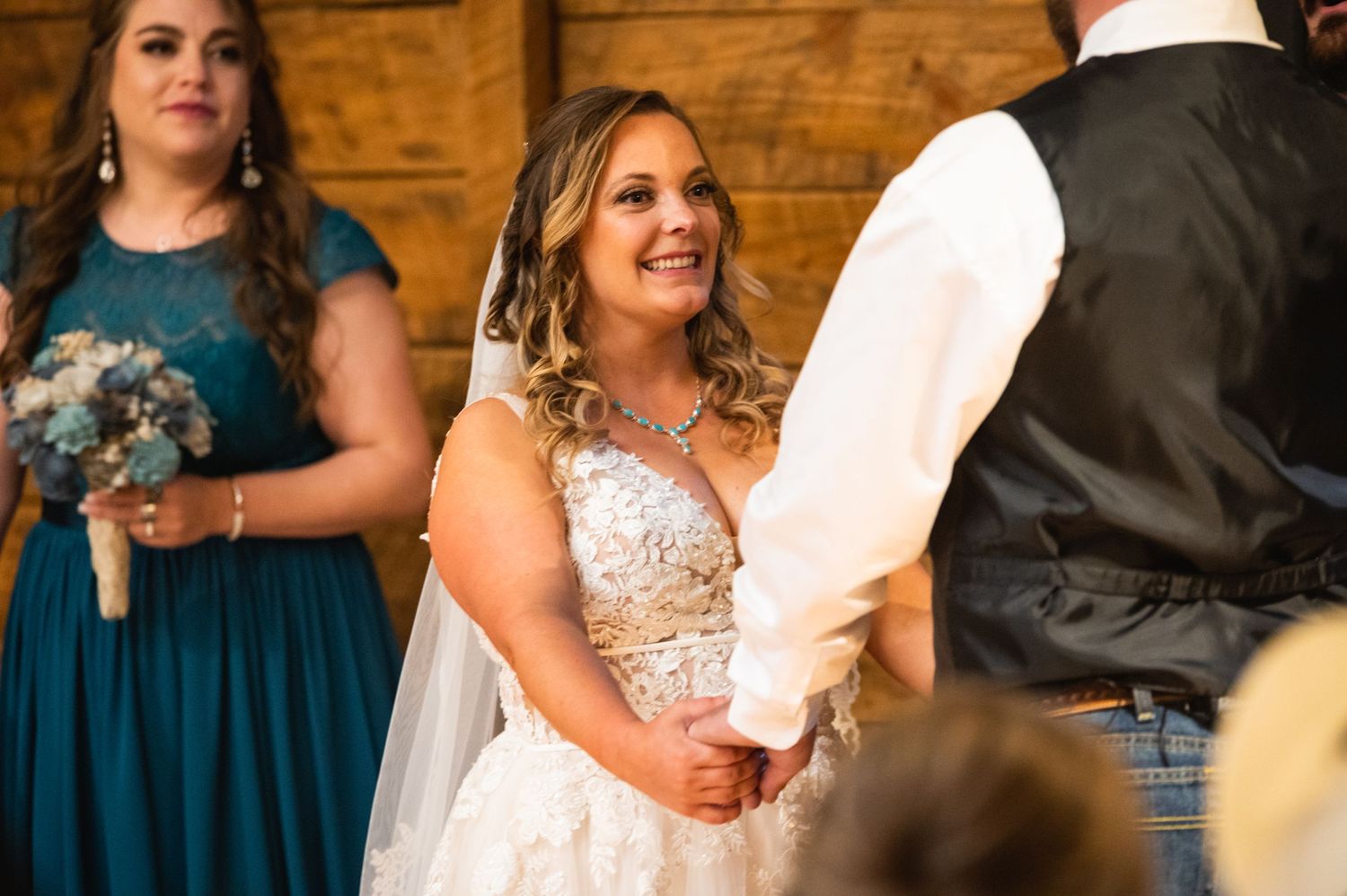 A wedding ceremony in a rustic barn venue with bridesmaids in teal dresses.