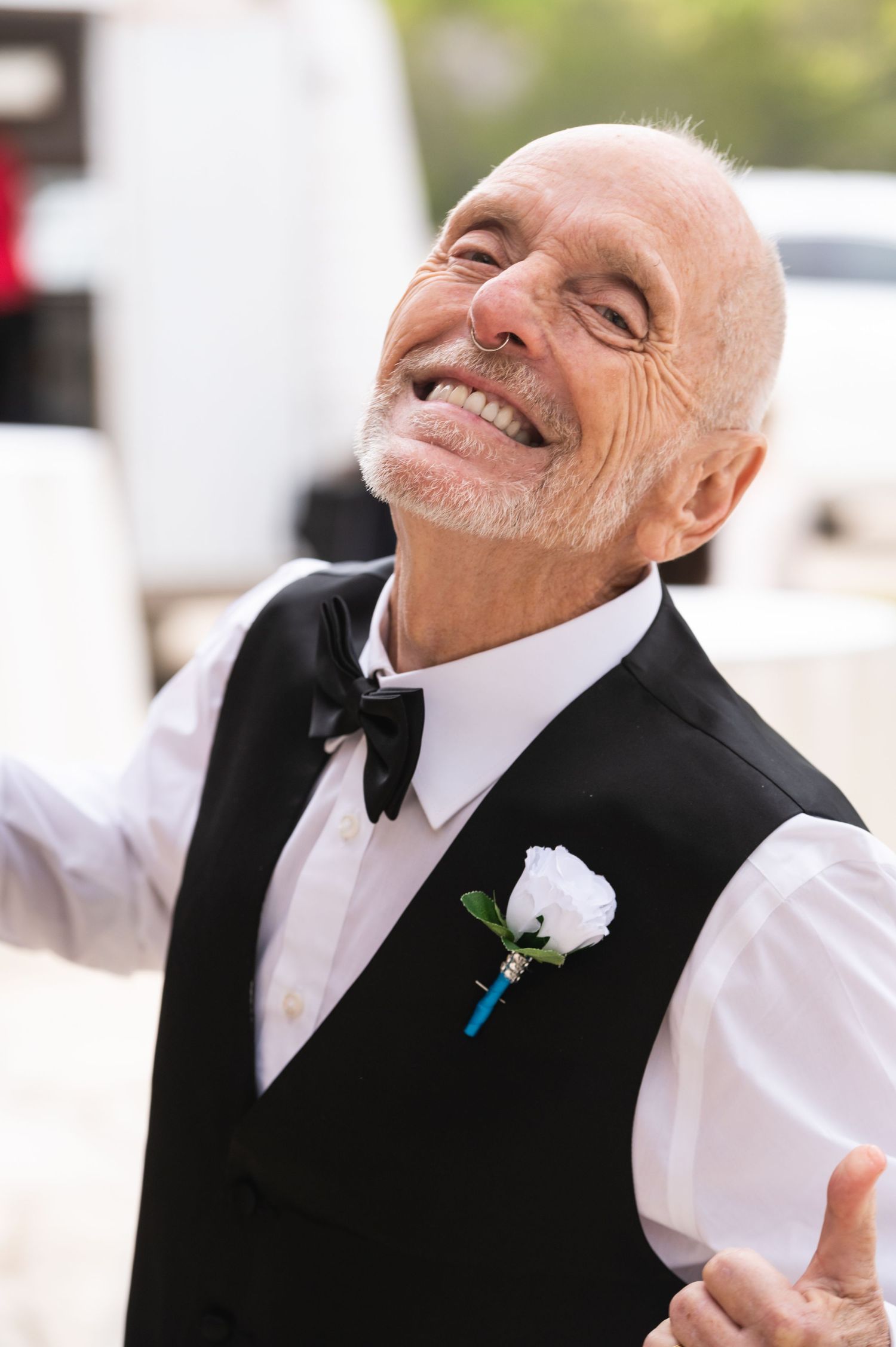 A happy senior man in formal attire with a white boutonniere and bow tie smiles joyfully.