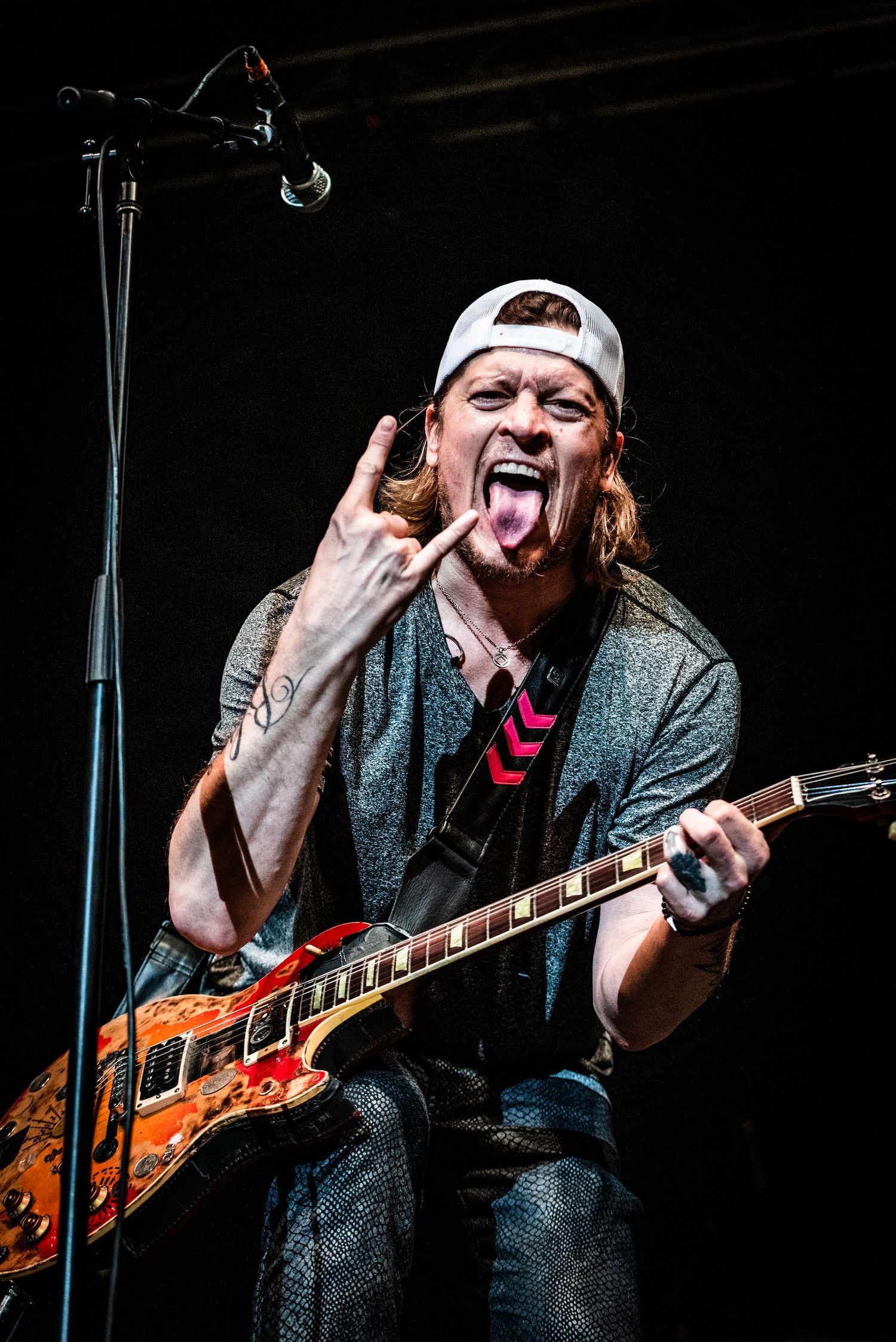 Energetic guitarist makes rock gesture while performing with custom painted guitar.