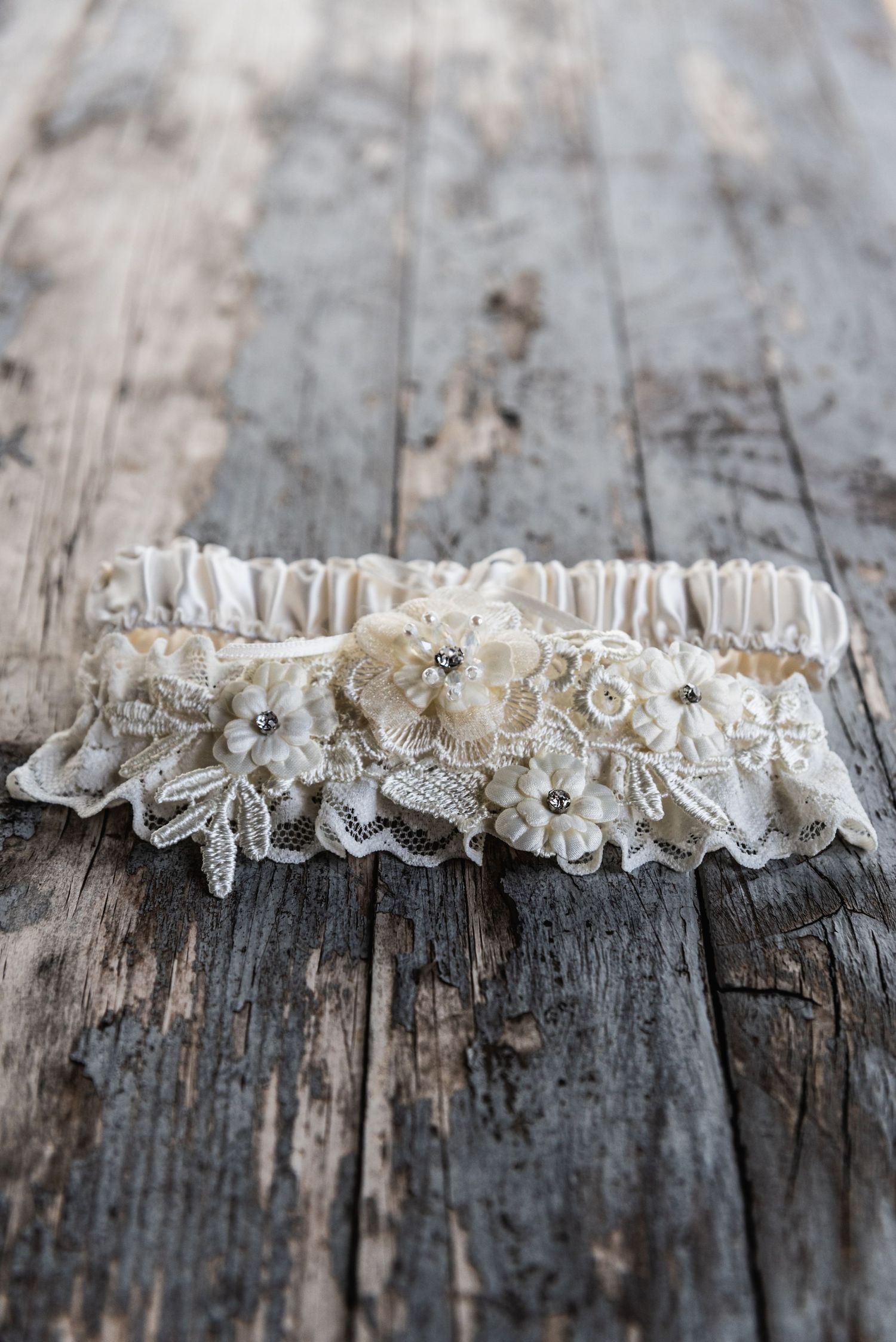 Vintage lace wedding garter with pearl details on rustic wooden surface.