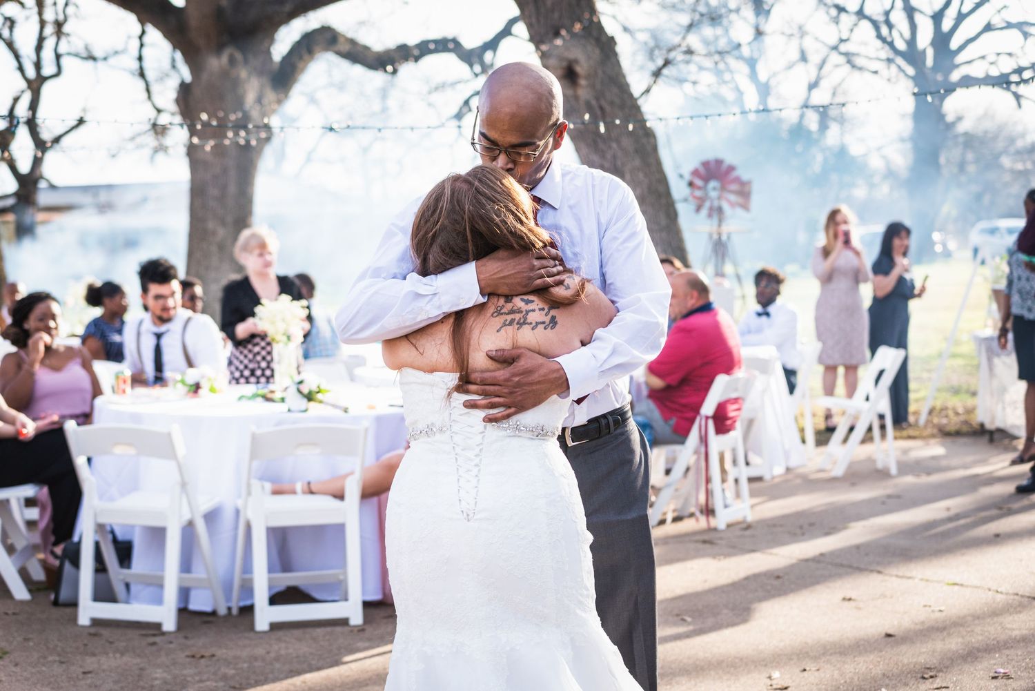 Romantic embrace during first dance at outdoor wedding reception with string lights and tables.