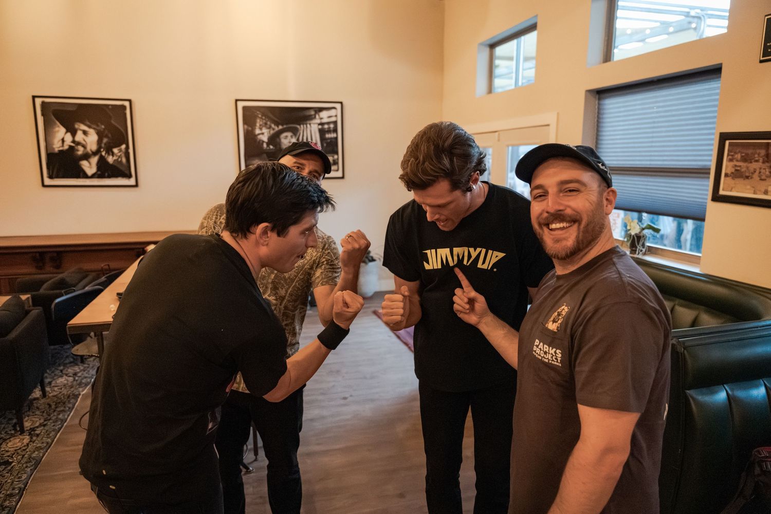 Three men laughing and comparing arm tattoos together inside a casual restaurant or bar setting.