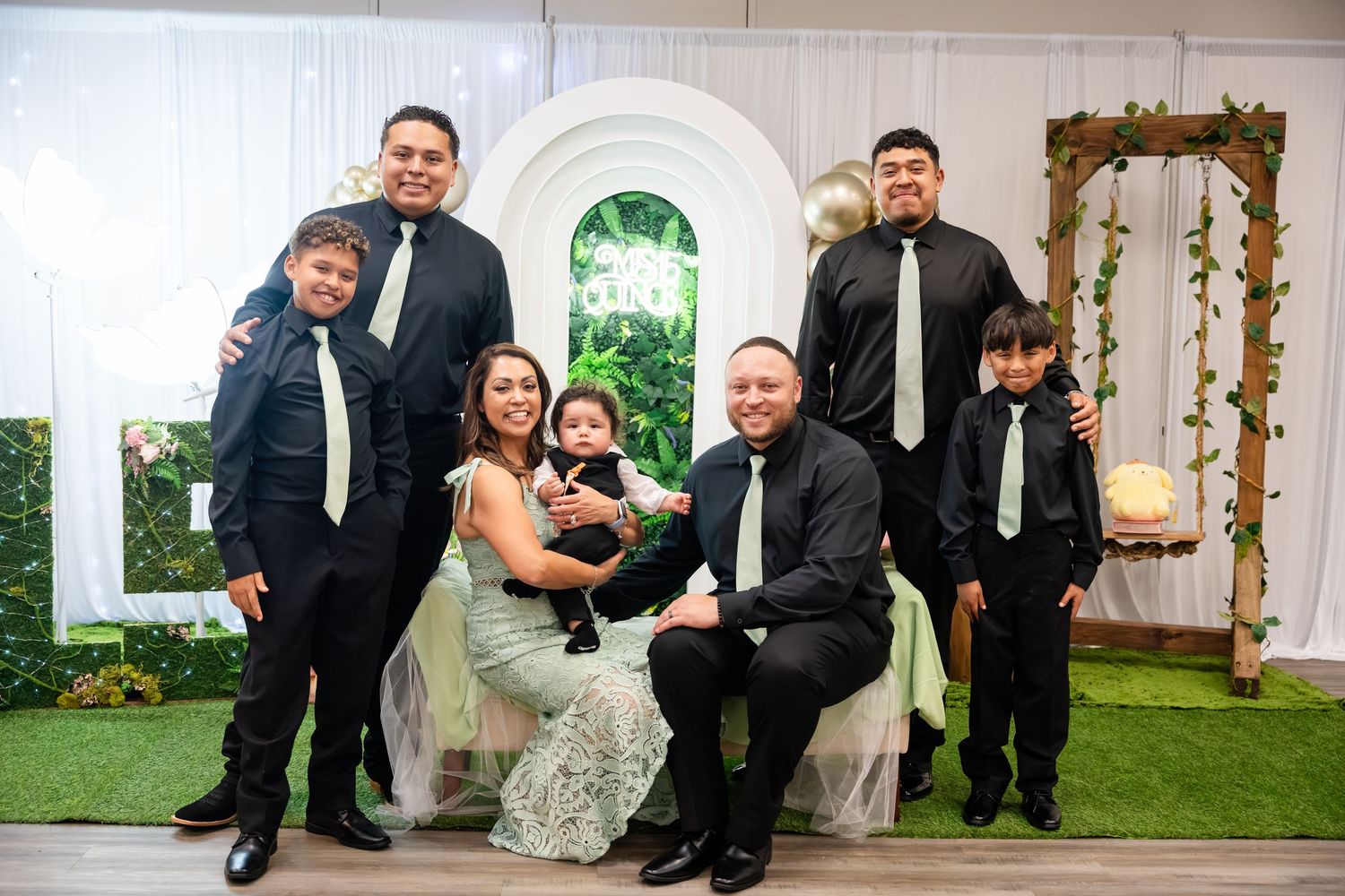 Family portrait at a formal event, dressed in black suits and elegant attire, posing together in a decorated venue.