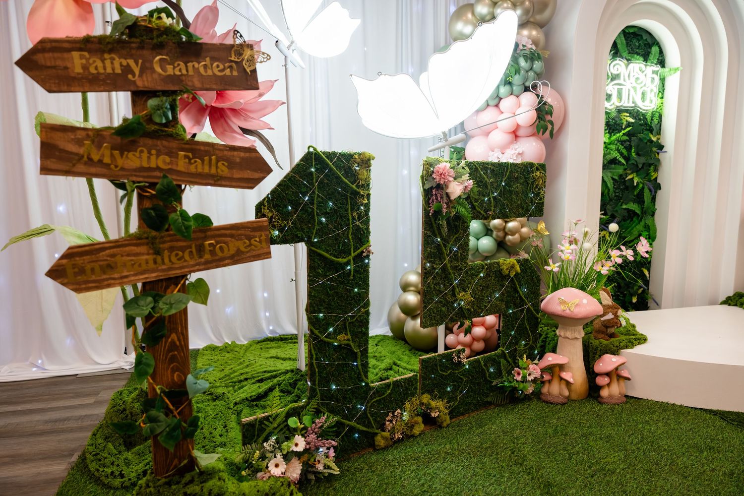 Fairy Garden birthday party decor with moss number 1, mushrooms, fairy signs, and pink floral balloon backdrop.