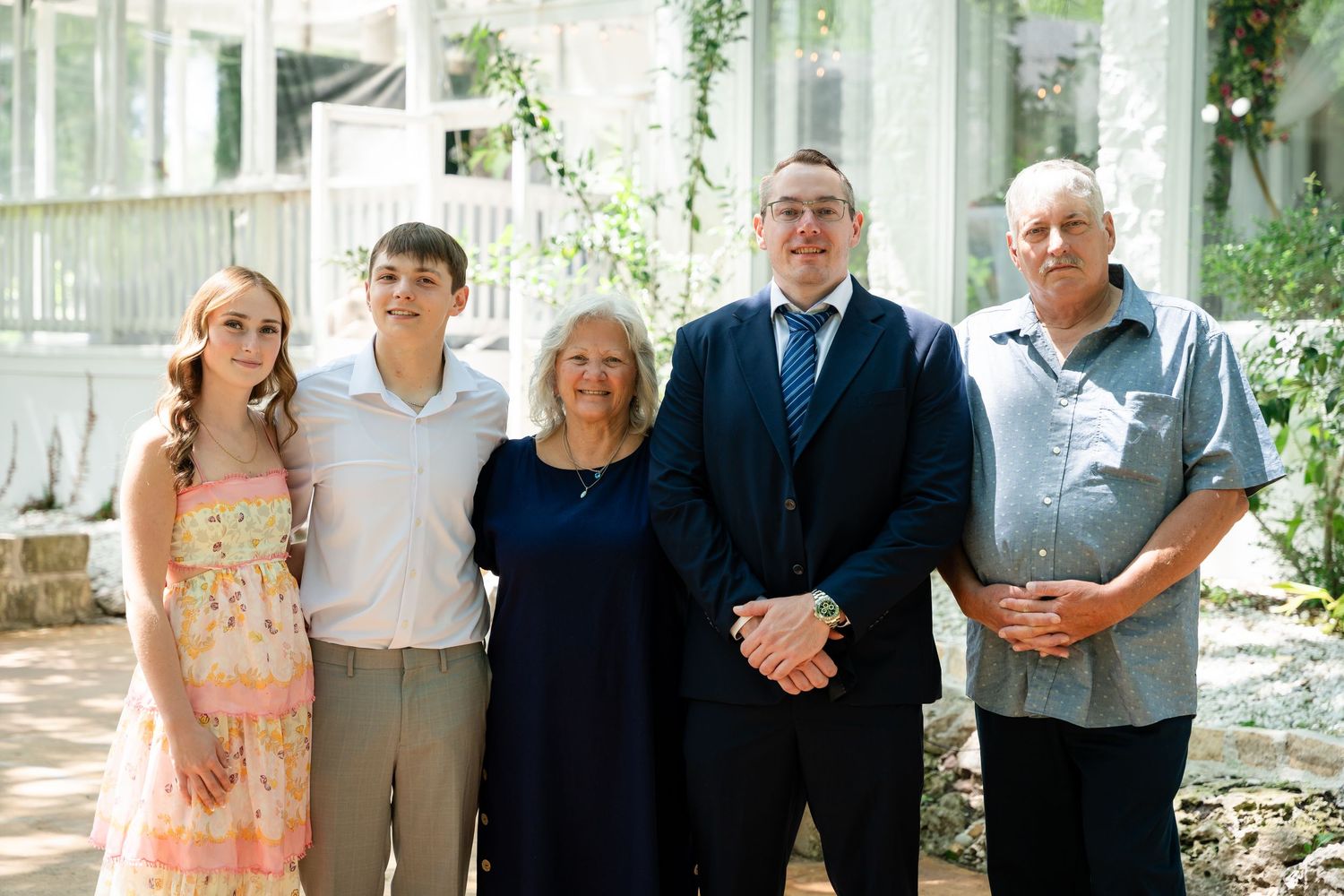 Family of five posing together outdoors near a greenhouse, dressed in formal and semi-formal attire for a special occasion.
