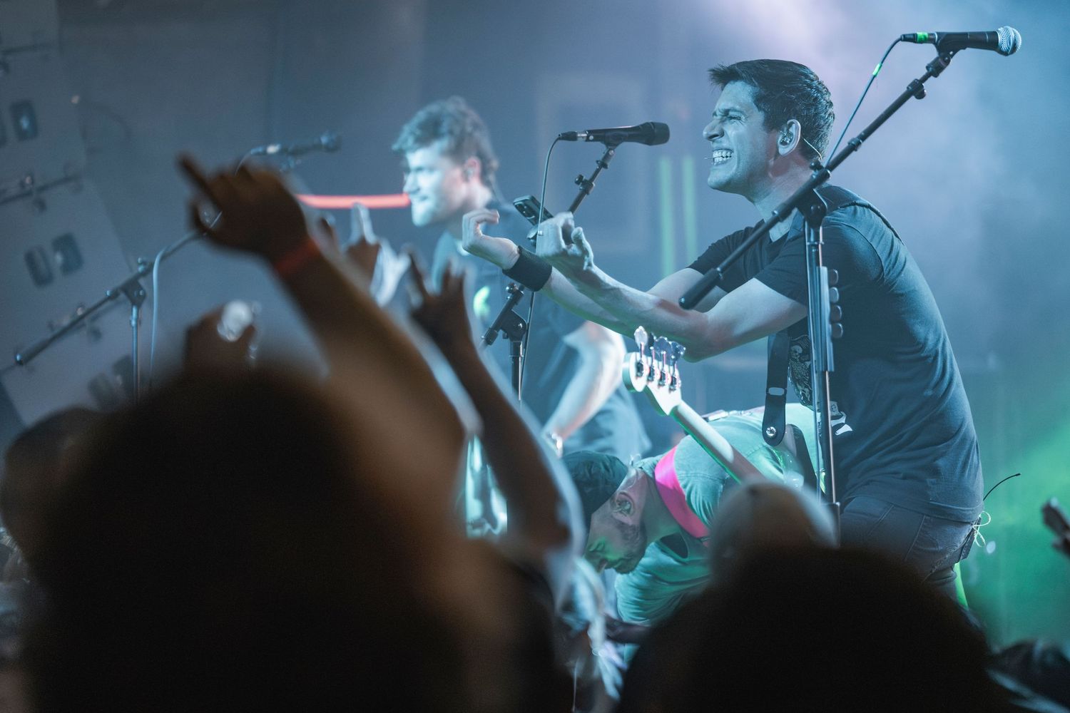 Musicians perform on stage with instruments under atmospheric blue and green lighting during a live concert.