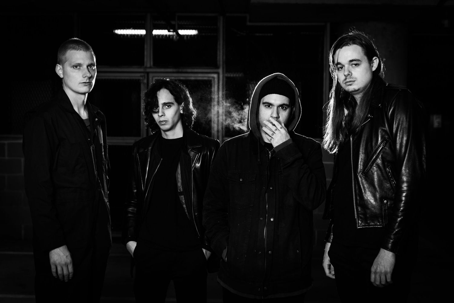A black and white collage of rock band members posing in dark clothing against a dark background.