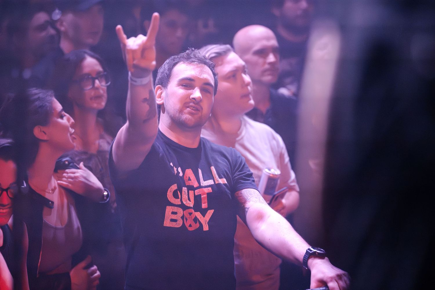 A concert attendee makes a rock gesture while enjoying the show under purple lighting.