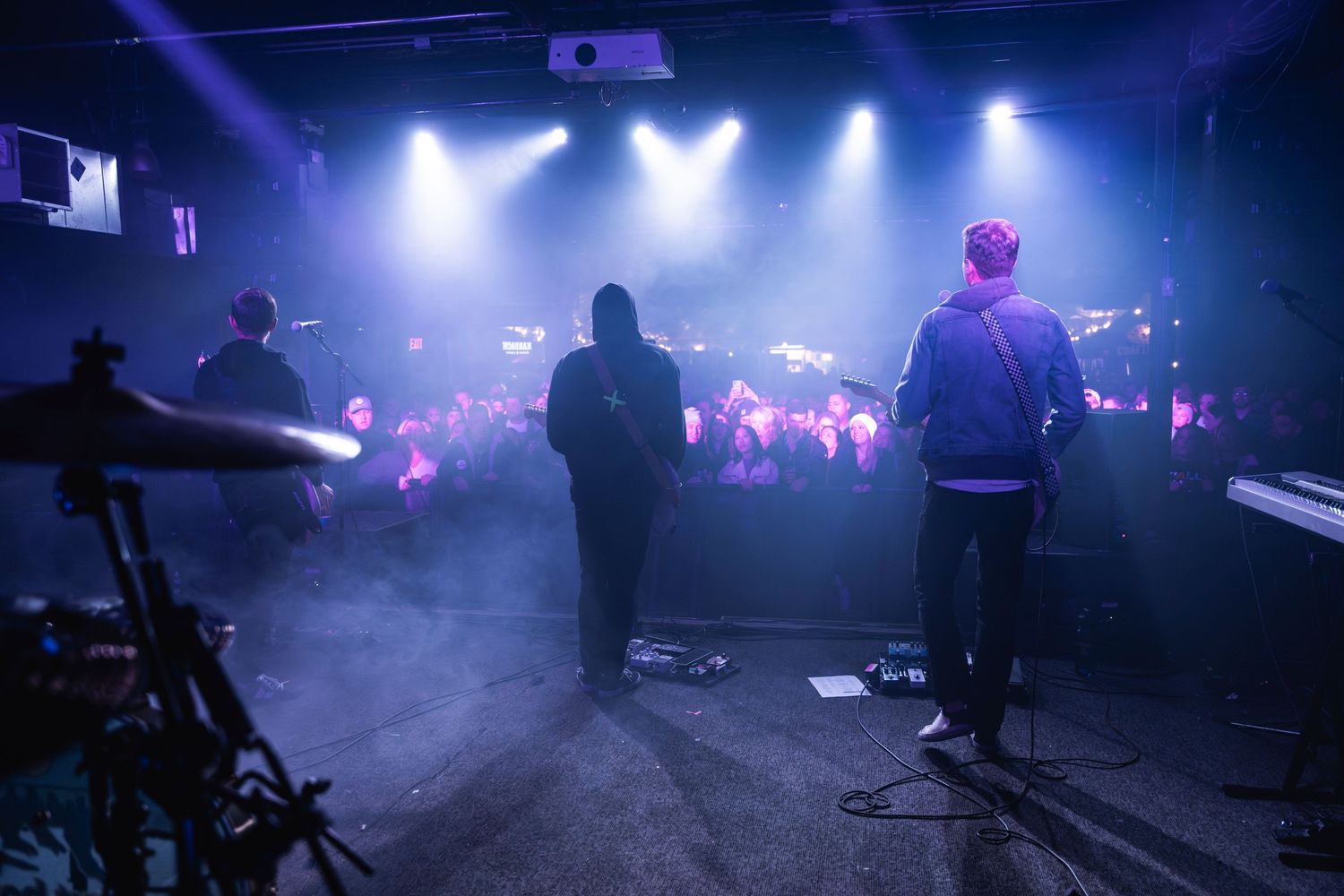 Band members performing on smoky stage with bright spotlights illuminating the crowd.